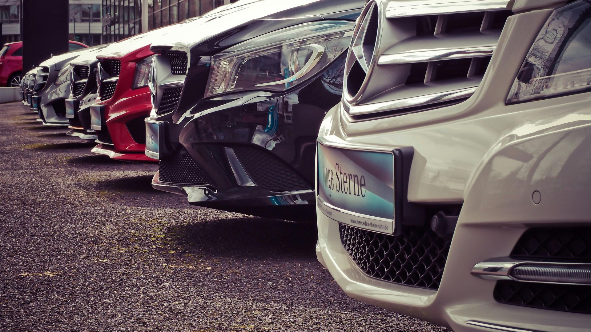 Cars parked in a row, including white, red, and black vehicles, displayed in a dealership lot.