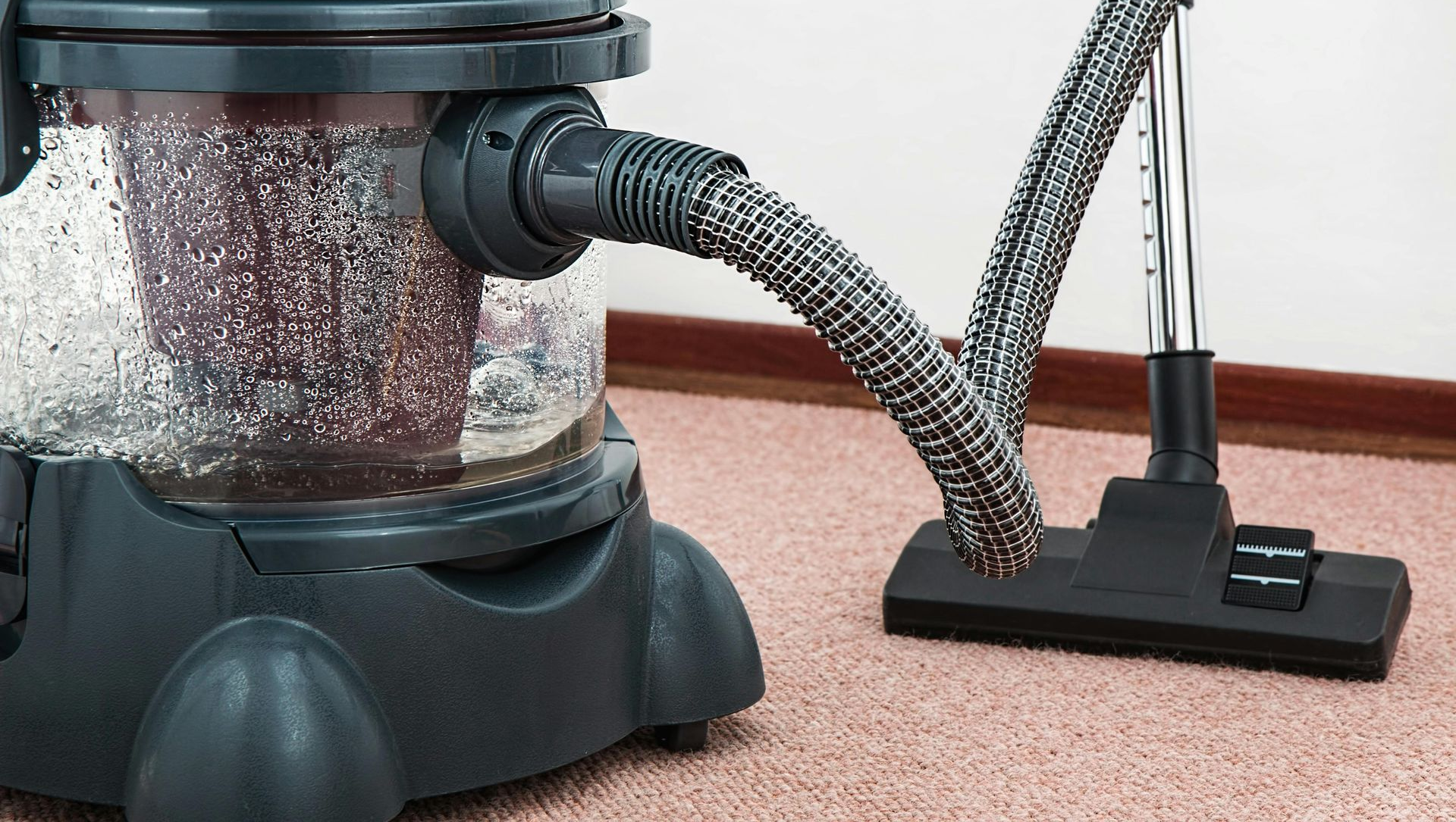 Red and black wet/dry vacuum cleaner, with hose and nozzle, on a carpet.