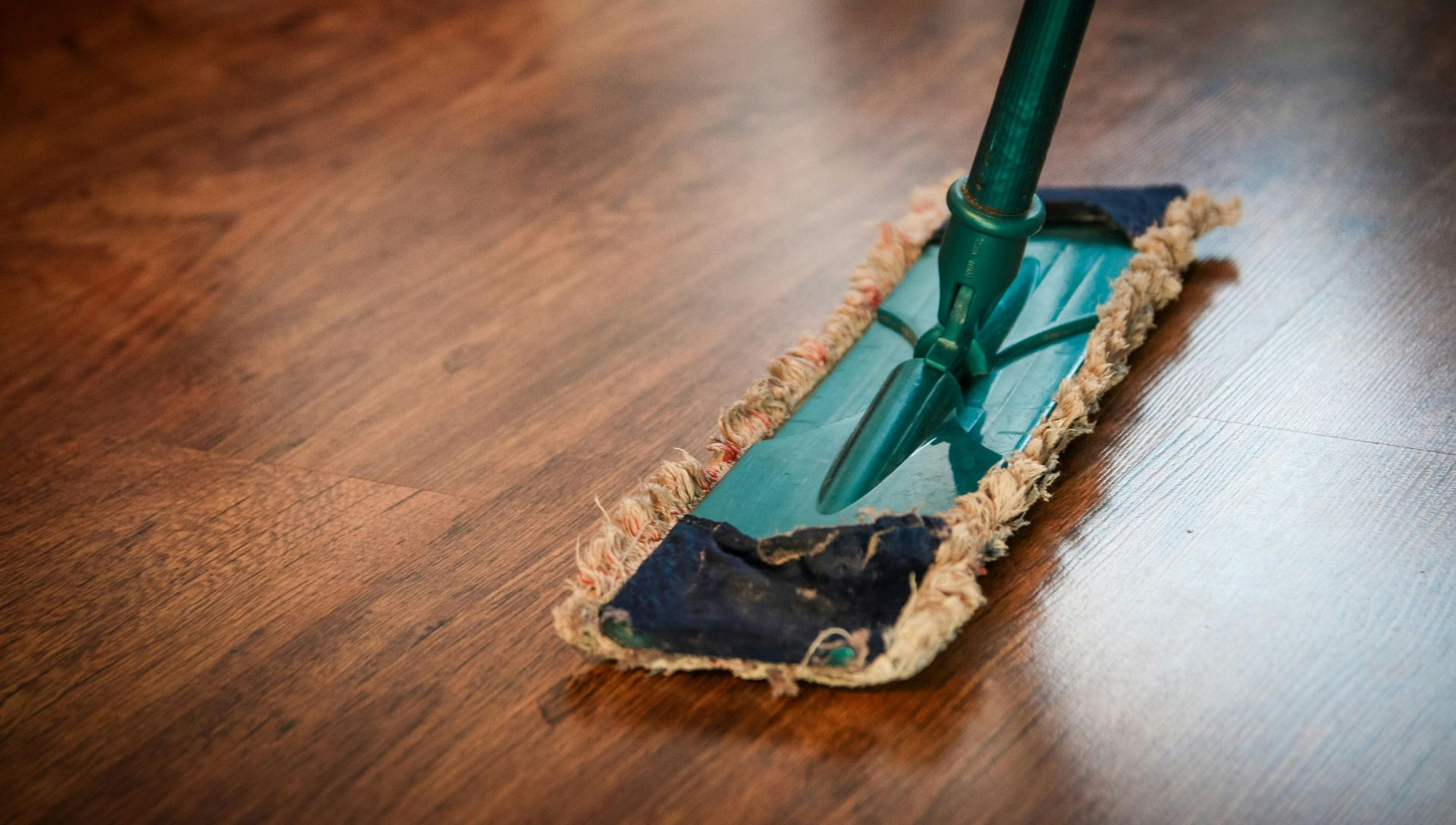 Mop cleaning a shiny brown hardwood floor. Green mop handle.
