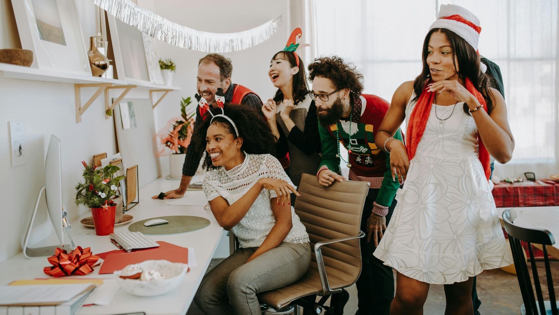 Office holiday party with coworkers gathered around a computer, decorated with festive cheer.