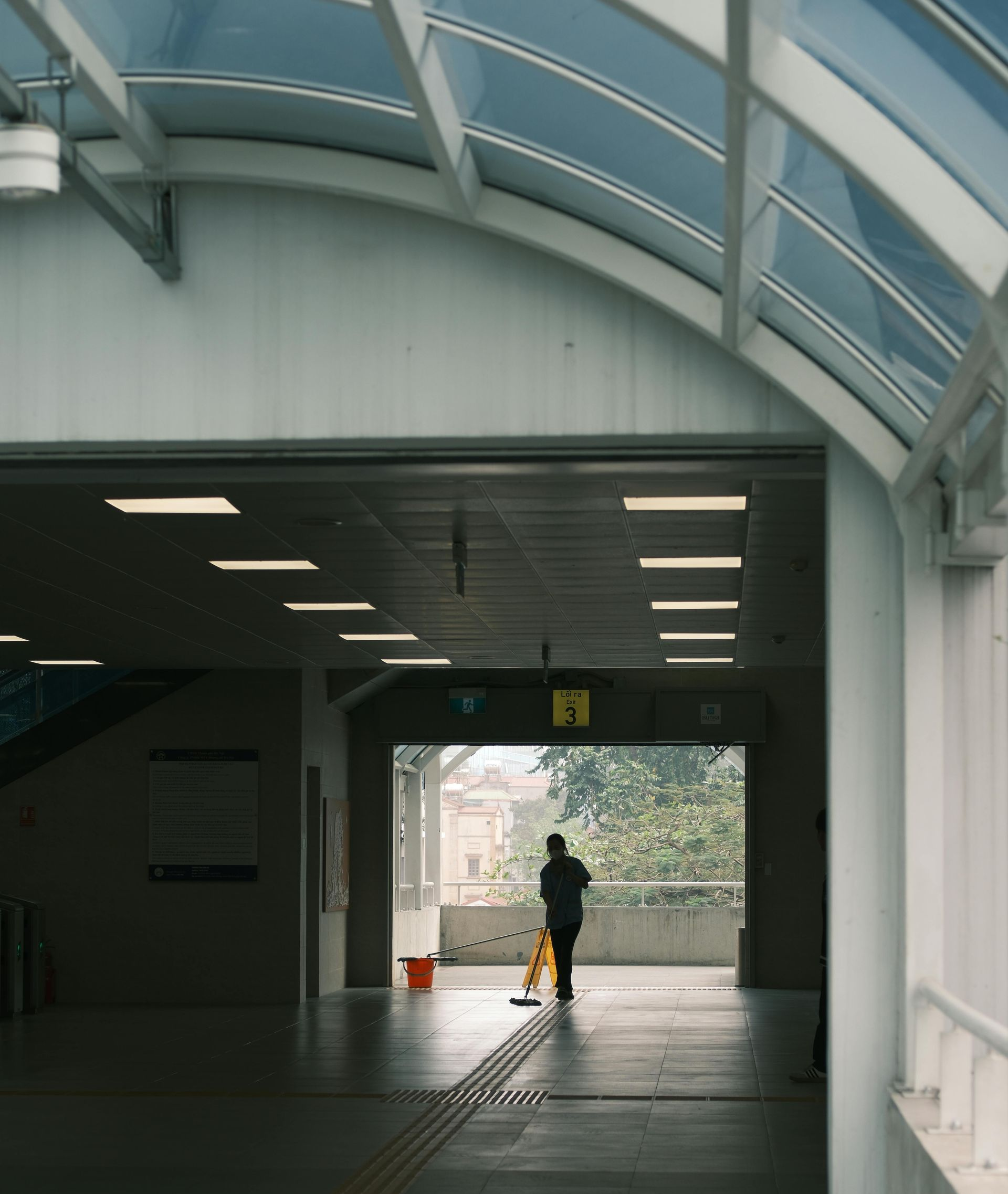 A person mops a brightly lit walkway with a view of greenery in the distance.