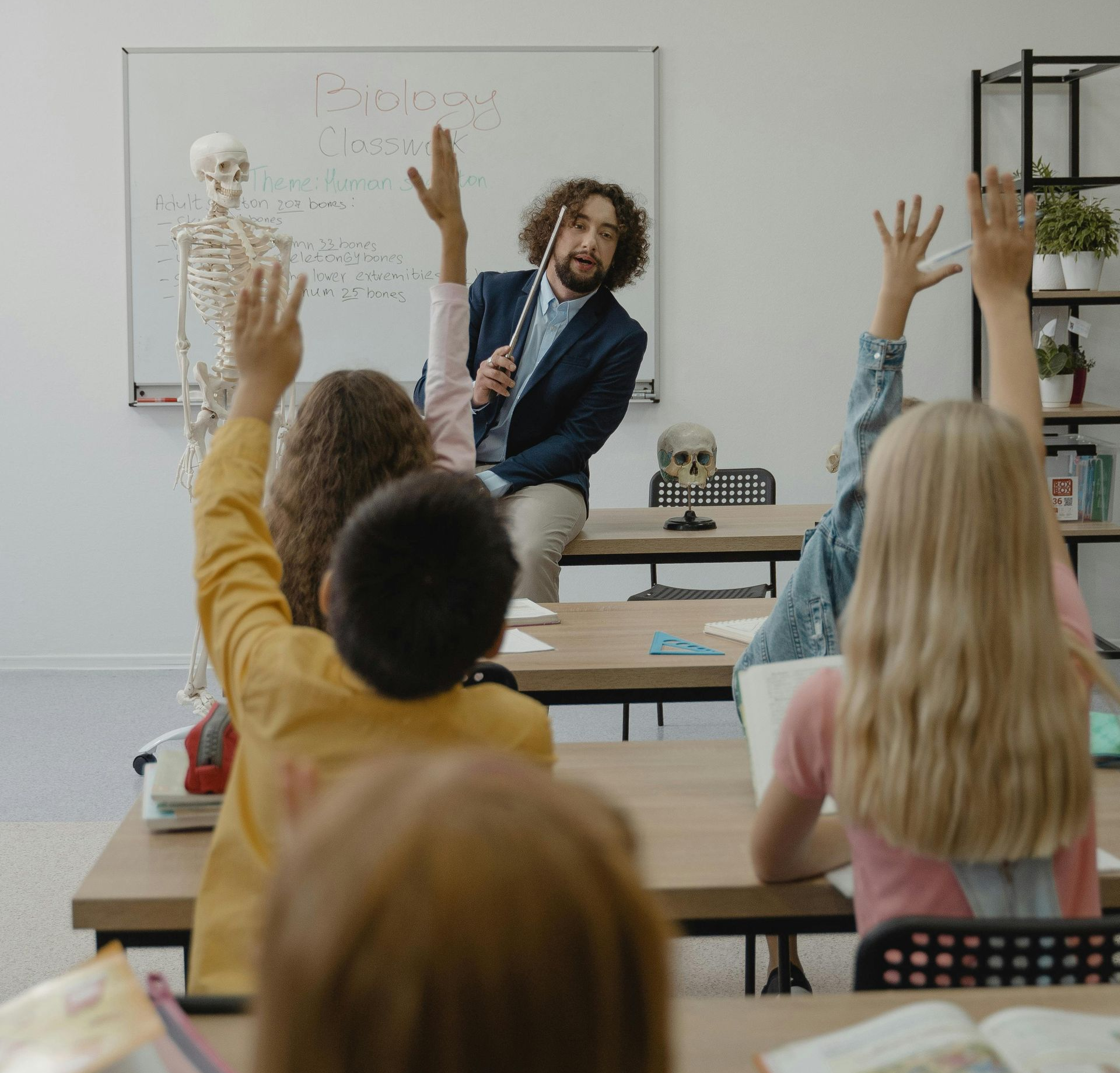 Teacher in a classroom with children raising their hands, skeleton on the wall.