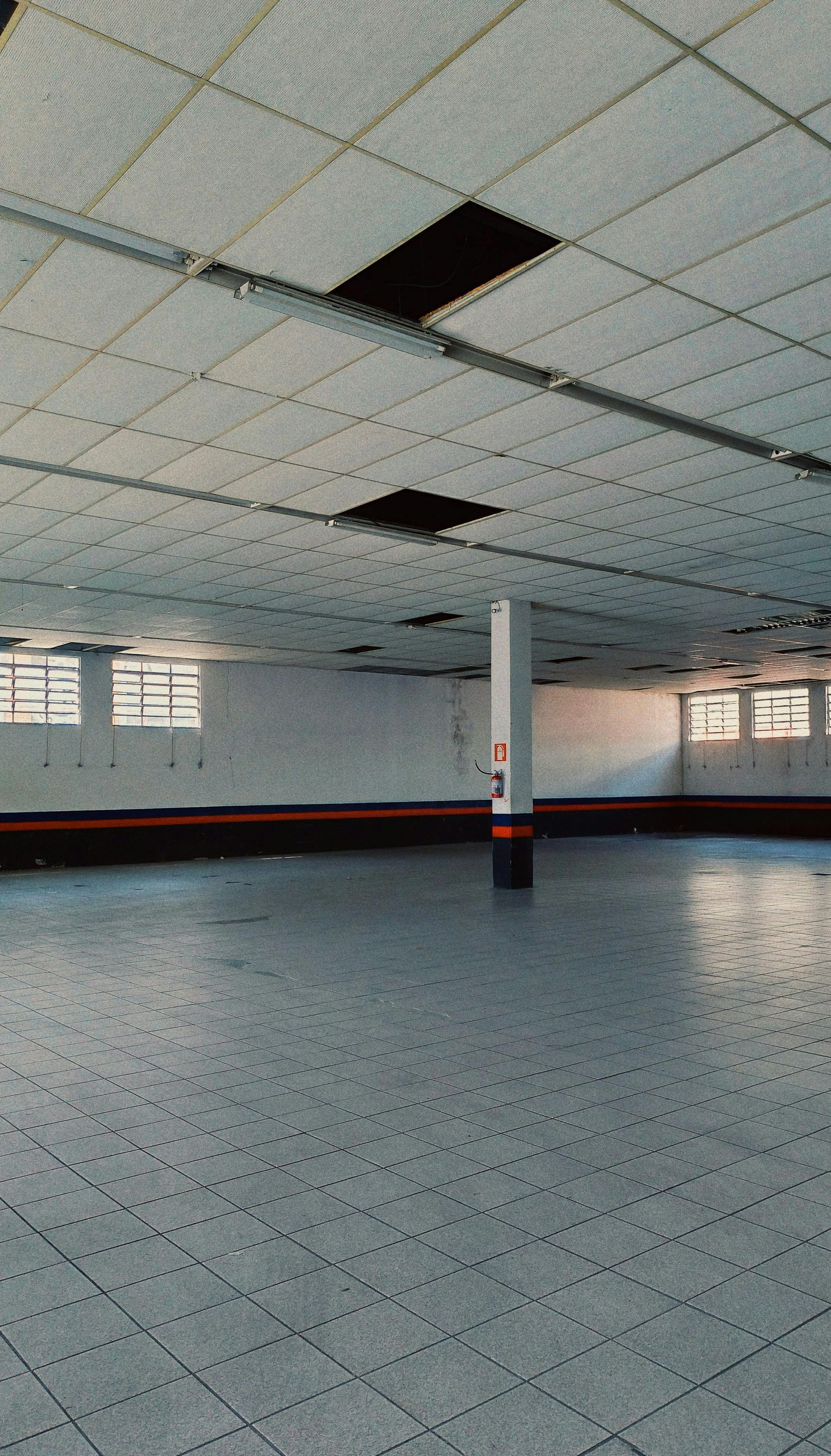 Empty indoor space with a tiled floor and ceiling, several windows, and a central pillar.