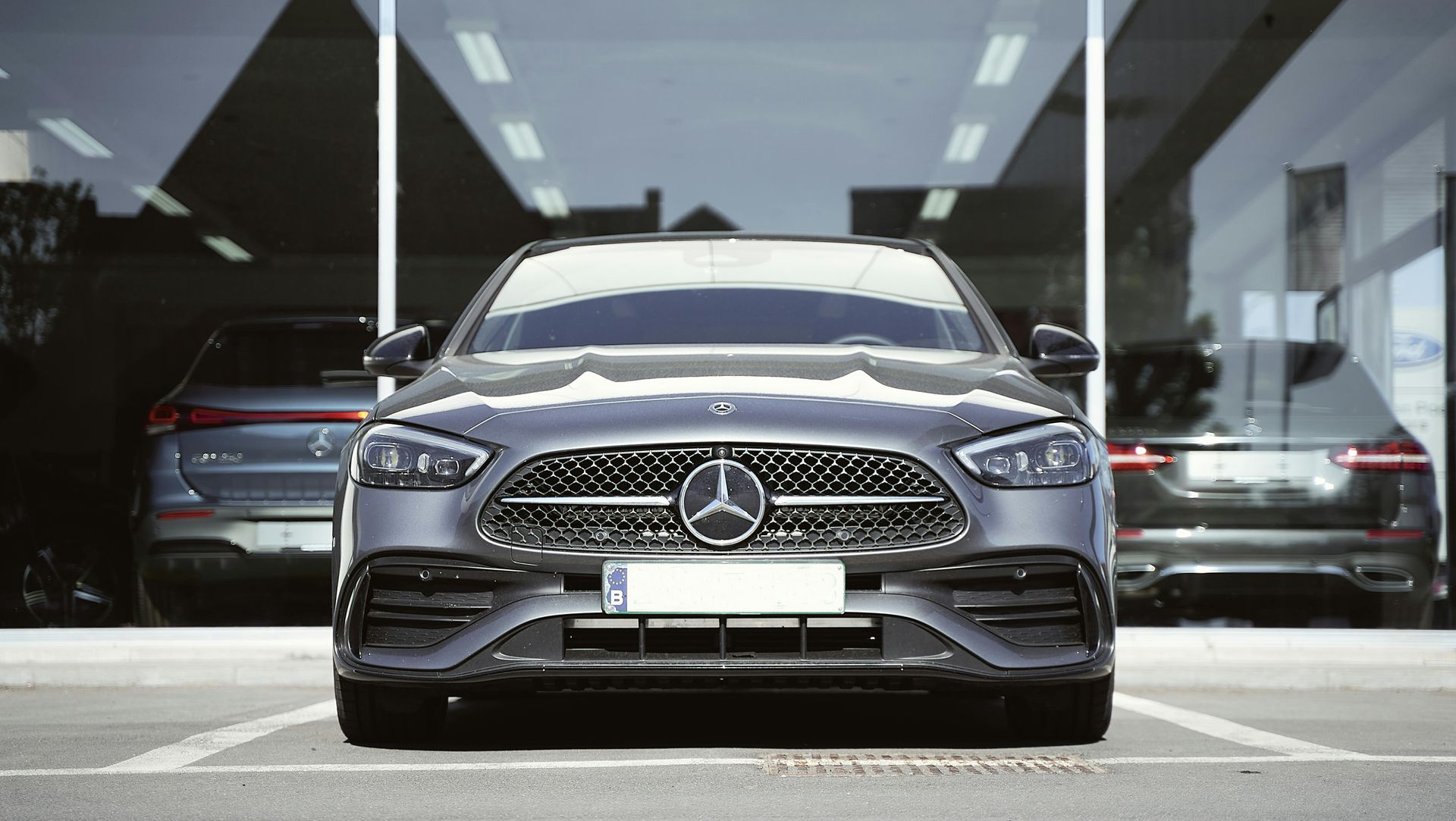 Gray Mercedes-Benz sedan parked in front of a glass-windowed dealership.