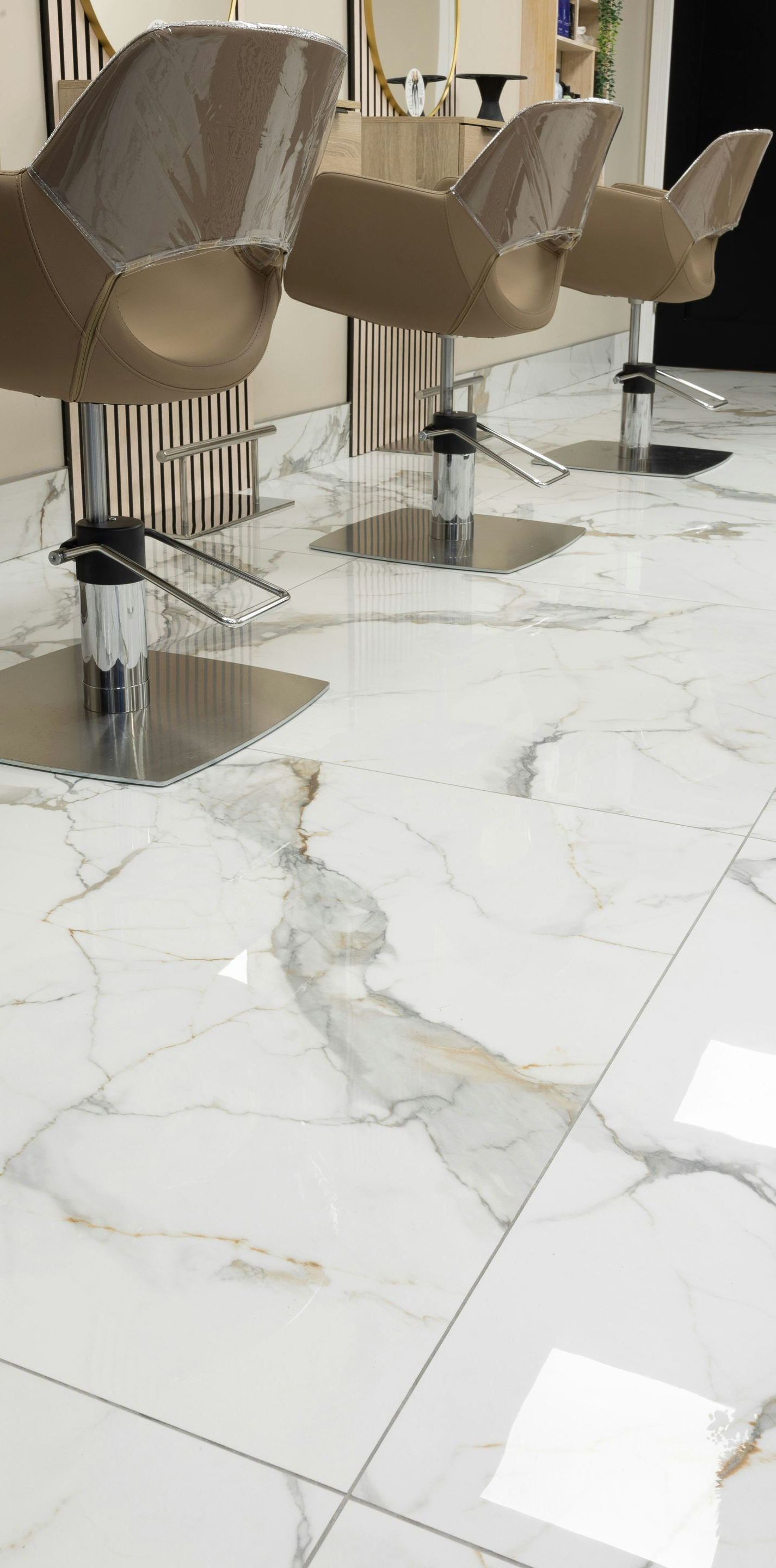 Salon interior with three tan chairs on metallic bases, white marble-style floor.