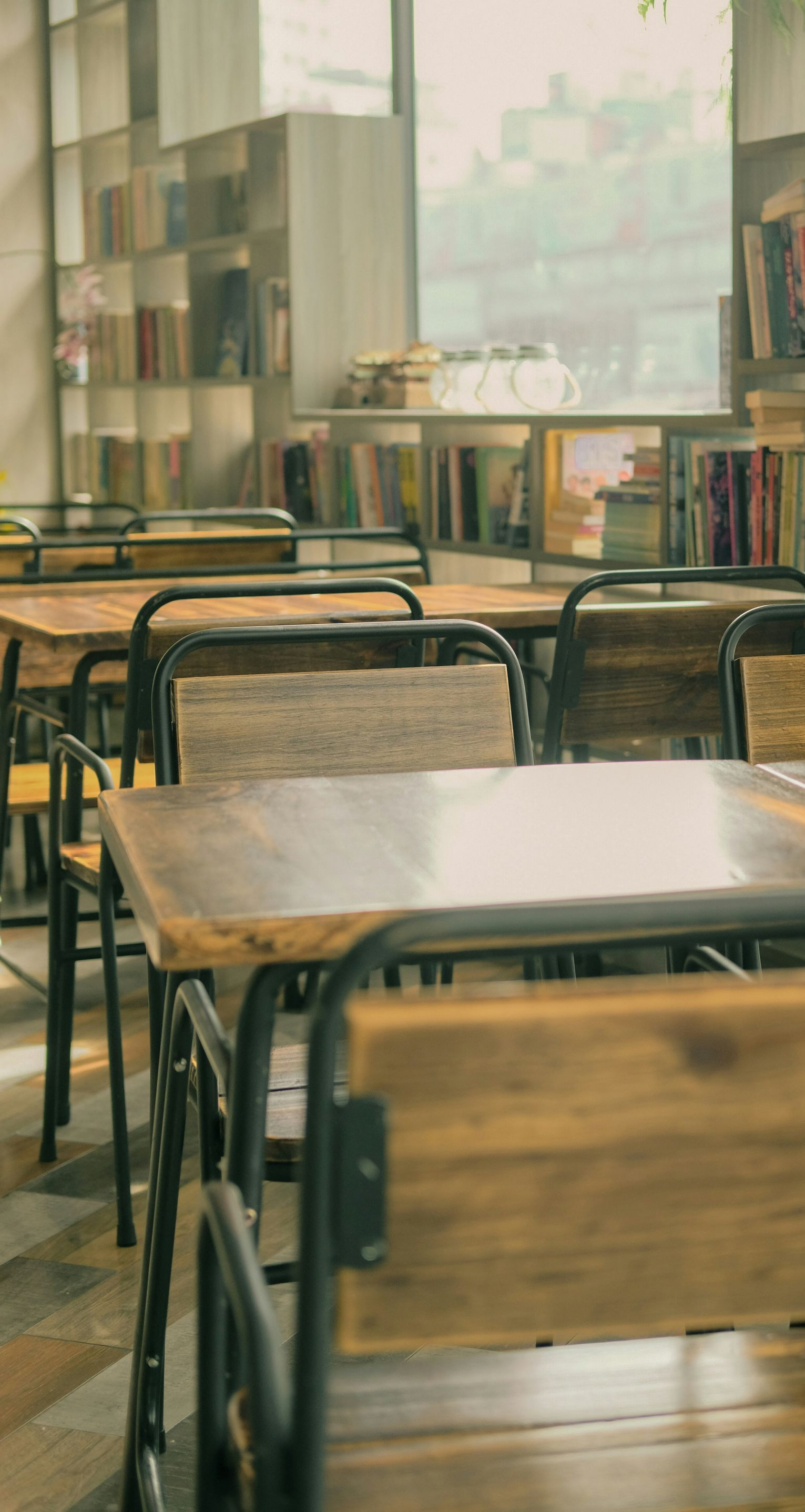 Wooden tables and chairs in a sunlit bookstore or cafe, shelves of books in the background.