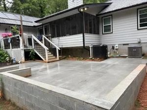 Concrete patio under construction beside a house with white siding and porch stairs.