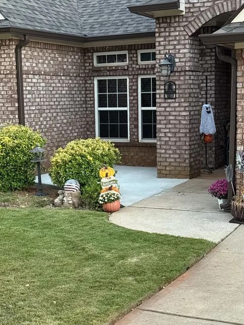 Brick house entryway with white-trimmed windows, concrete walkway, and lawn with fall decorations