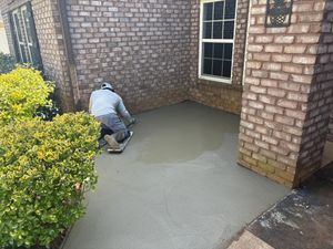Worker smoothing wet concrete beside a brick house and window.