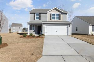 Suburban two-story house with attached garage, concrete driveway, and dry front lawn under a partly cloudy sky