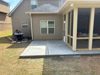 Backyard patio with concrete slab and screened porch beside a tan house