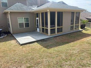 Rear view of a beige house with screened porch, concrete patio, and a dry grass backyard