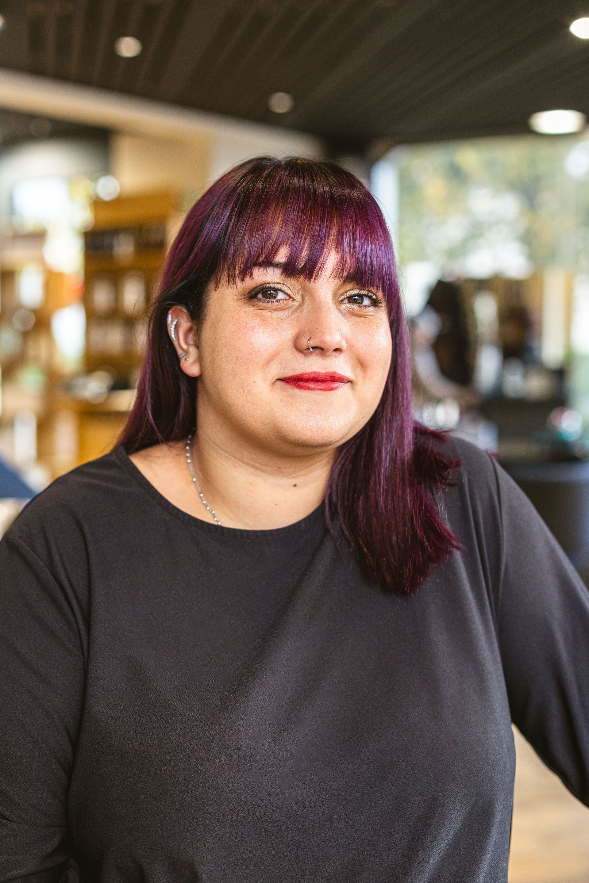 Une femme aux cheveux violets et aux lèvres rouges porte une chemise noire.
