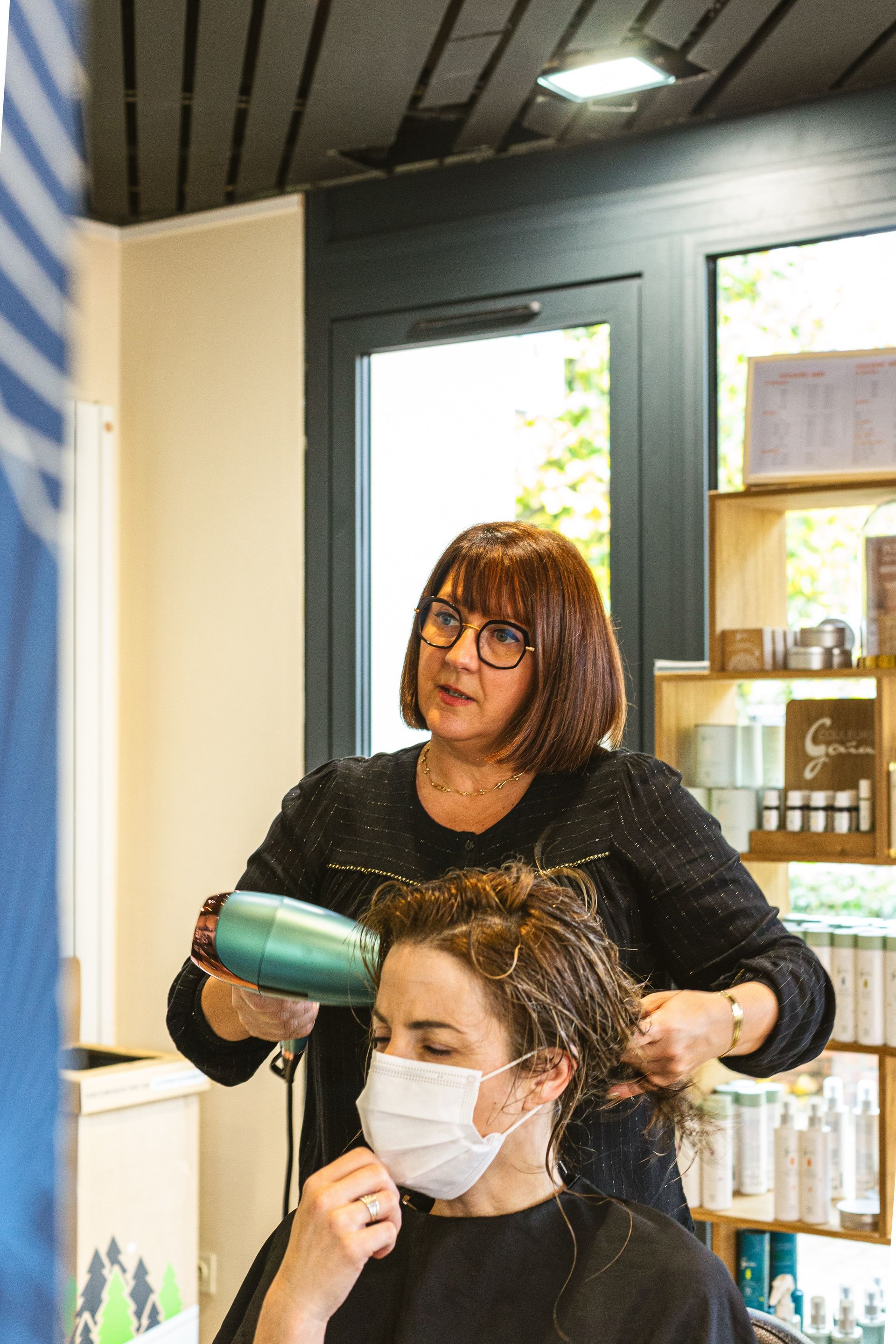 Une femme portant un masque se fait sécher les cheveux par un coiffeur.