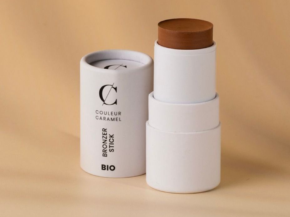 Un tube de bronzer stick couleur caramel est posé sur une table.