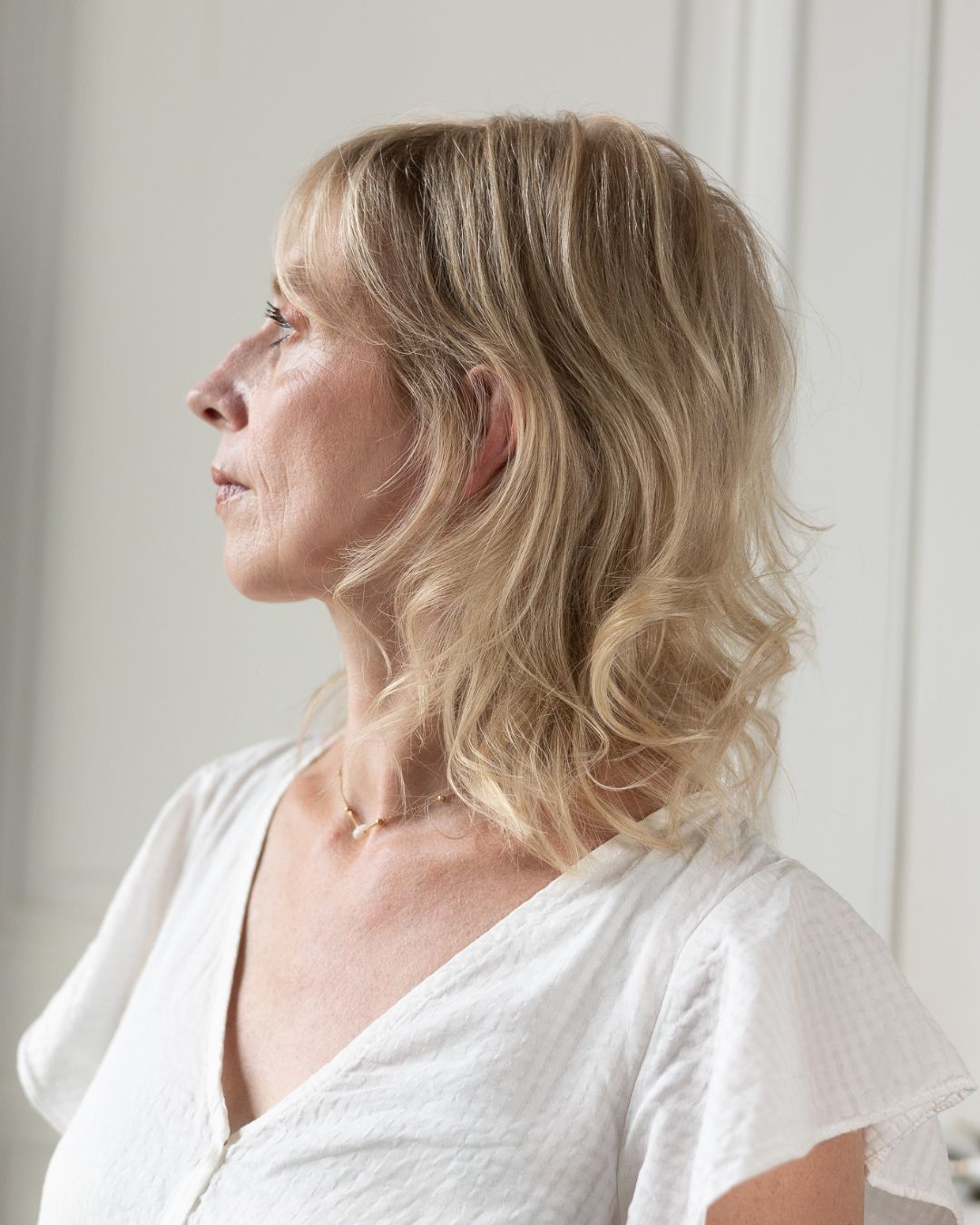 Une femme aux cheveux blonds porte une chemise blanche et un collier.