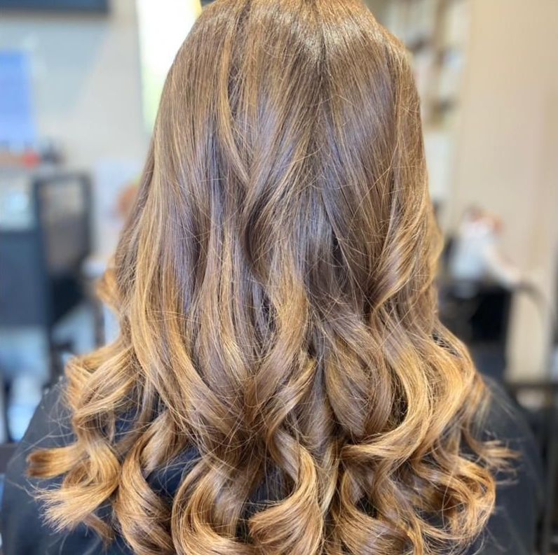 Une femme aux longs cheveux bruns est assise sur une chaise dans un salon.