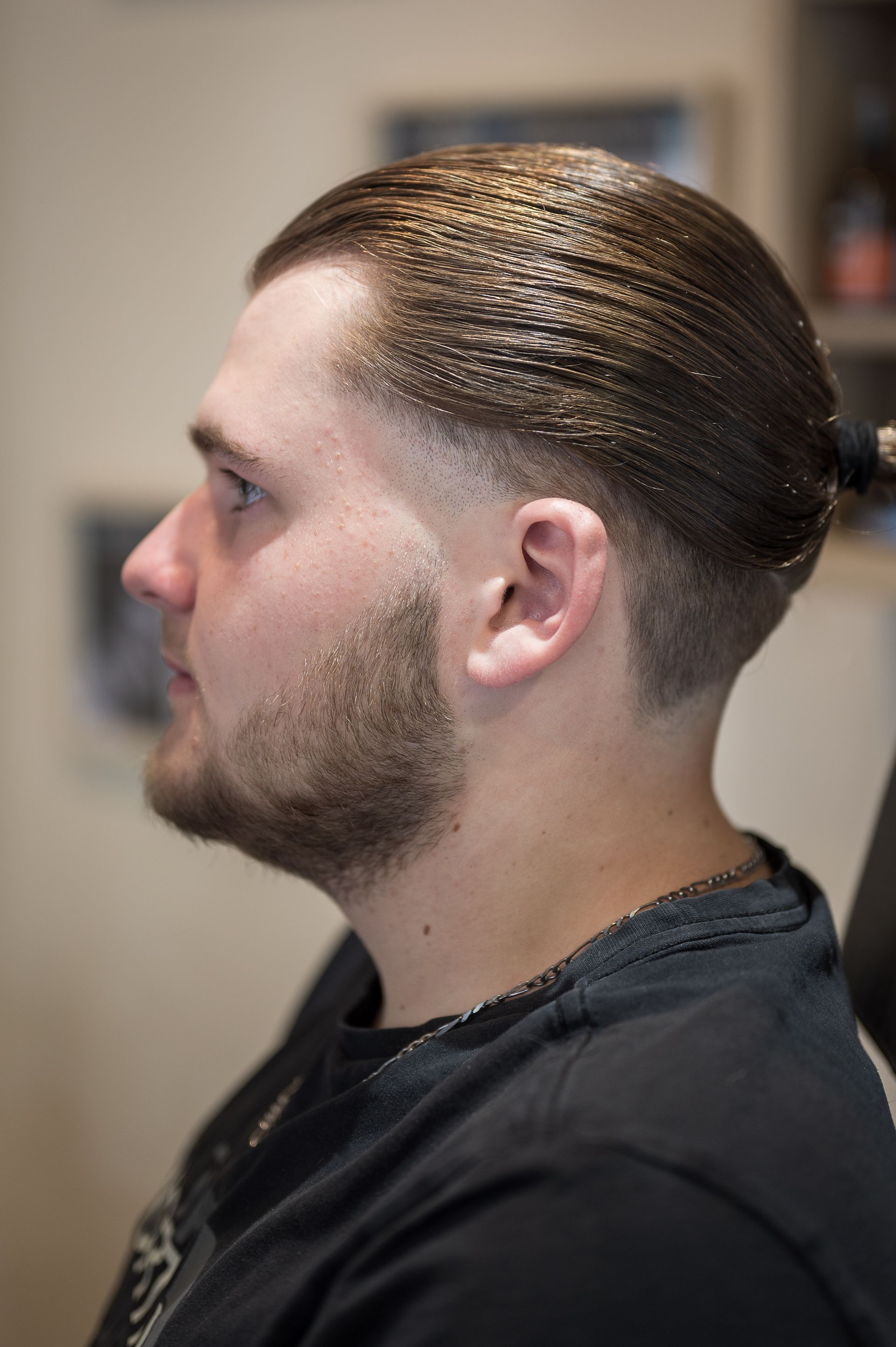 Un homme avec une barbe est assis sur une chaise avec ses cheveux en chignon.
