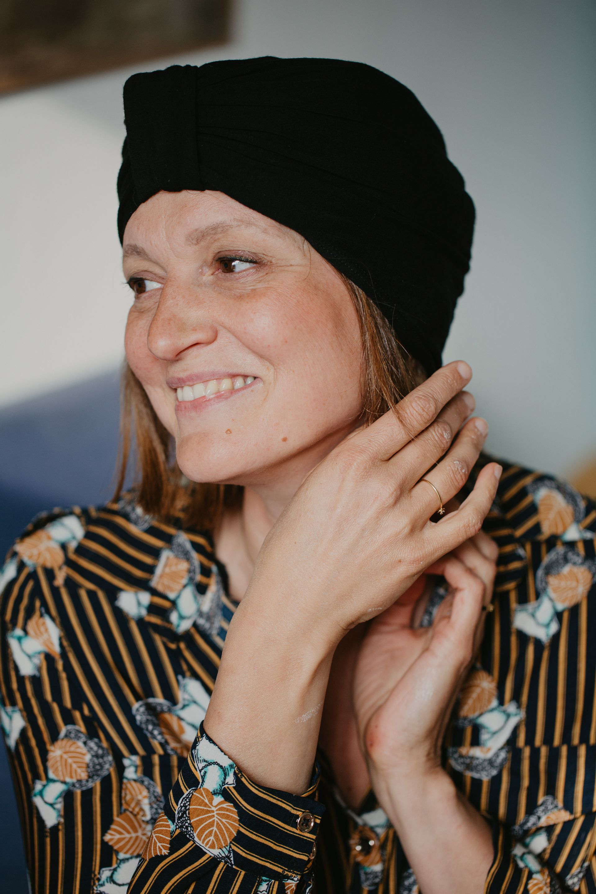 Une femme portant un chapeau noir et une chemise rayée sourit.