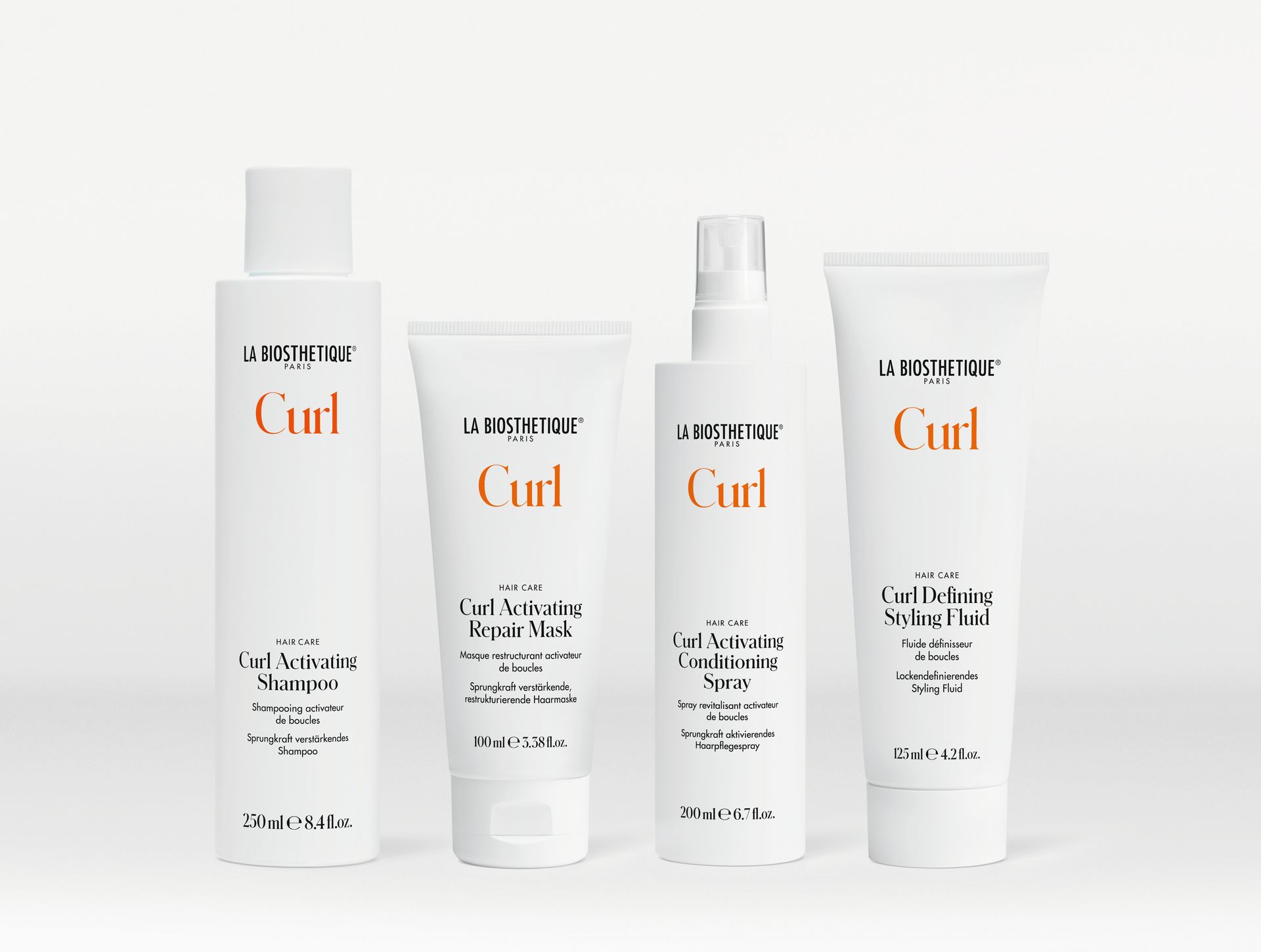 Quatre bouteilles de produits pour boucles sont alignées sur une surface blanche