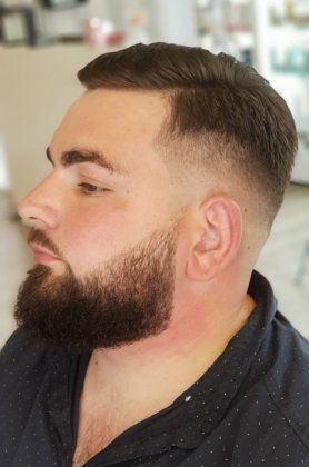 Un homme avec une barbe et une coupe de cheveux décolorée porte une chemise noire.