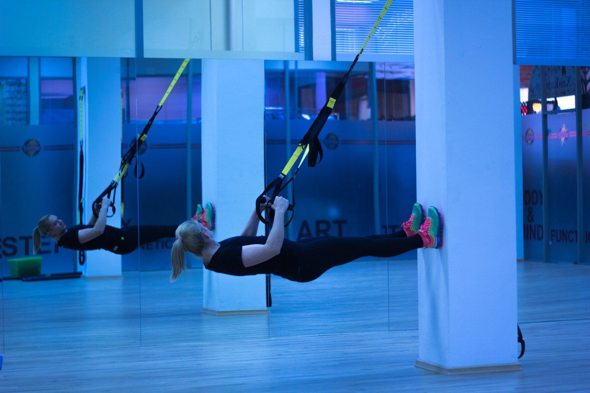 Two women are doing trx exercises in a gym.