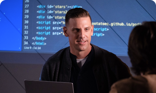 Man presenting code to someone, with code projected on a screen.