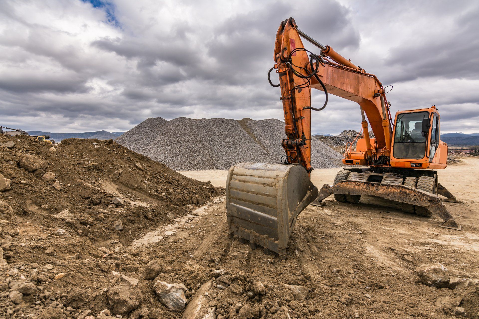 Une grande excavatrice orange est assise au sommet d'un champ de terre.