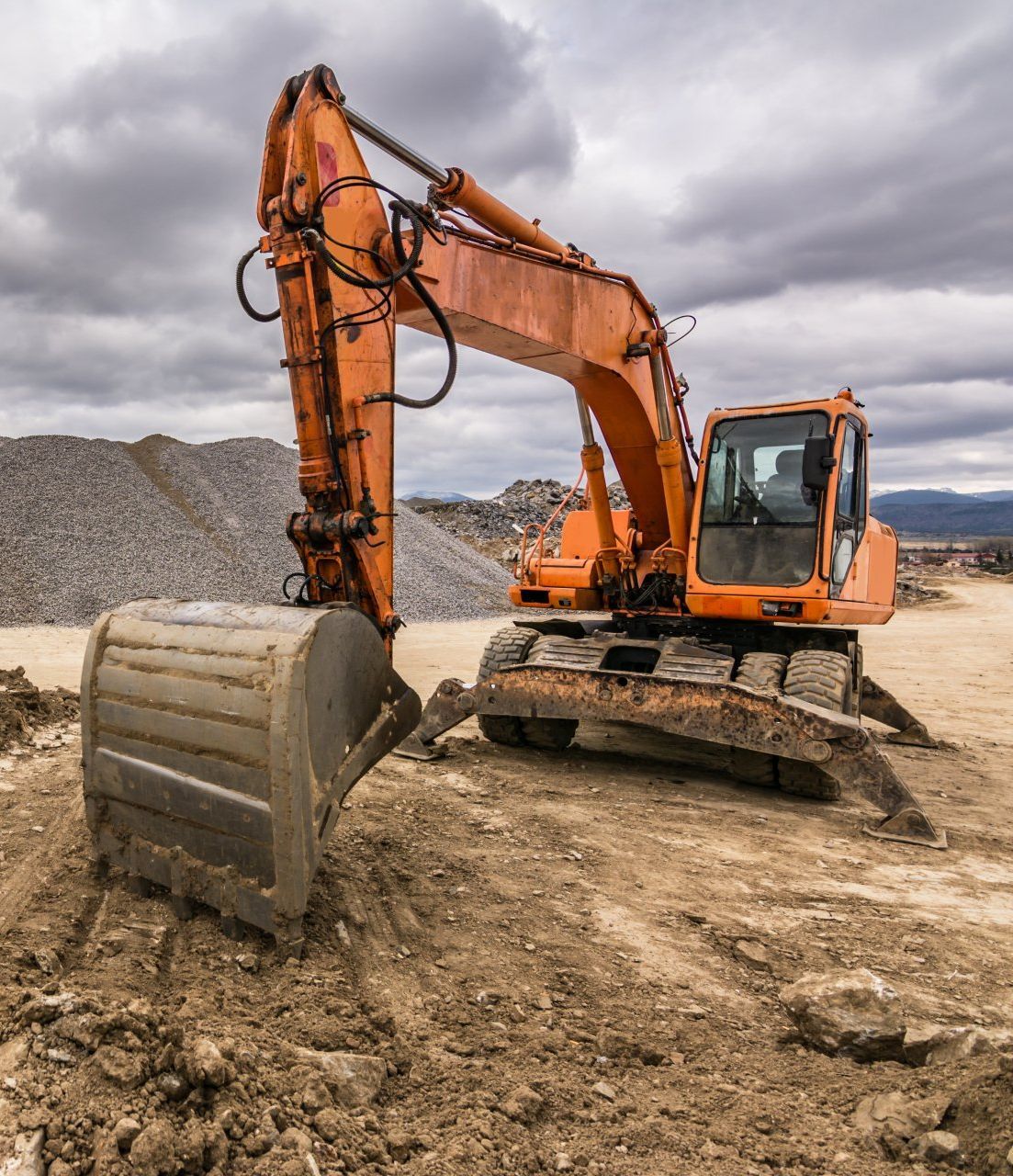 An orange excavator is sitting on top of a dirt field.