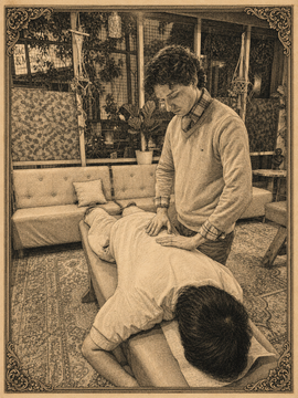 Therapist pressing a client’s back on a massage table in a pink treatment room