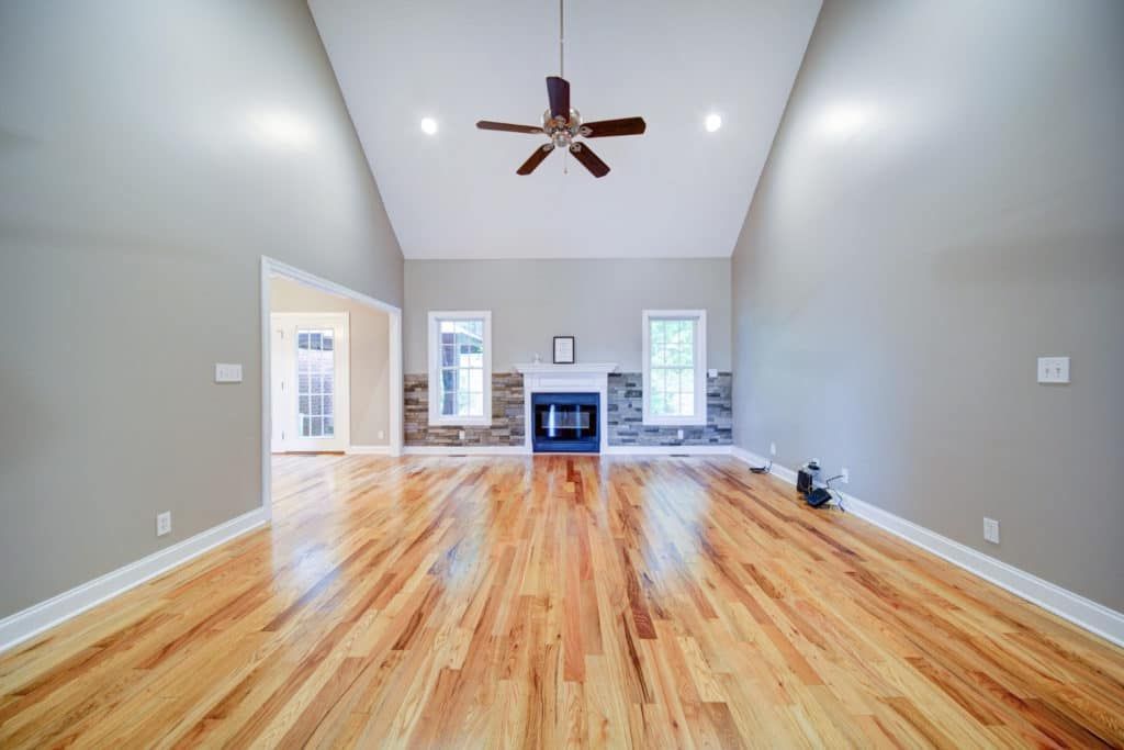 Empty living room with hardwood floors, fireplace, and high ceiling with a ceiling fan.