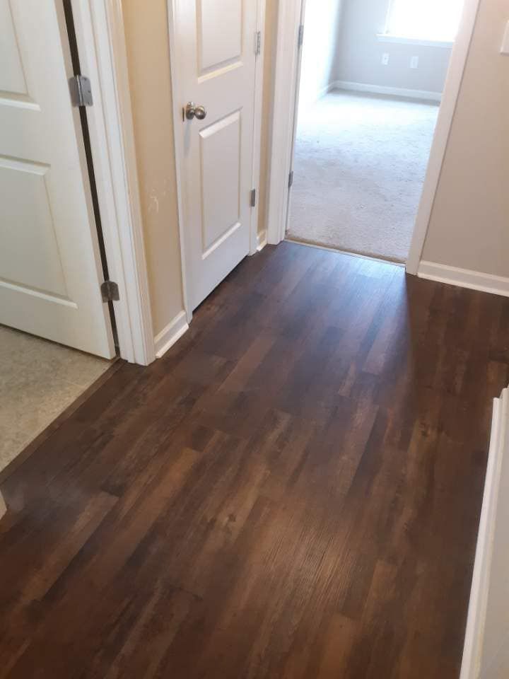 Dark wood flooring in hallway, leading to a room with carpet and two white doors.