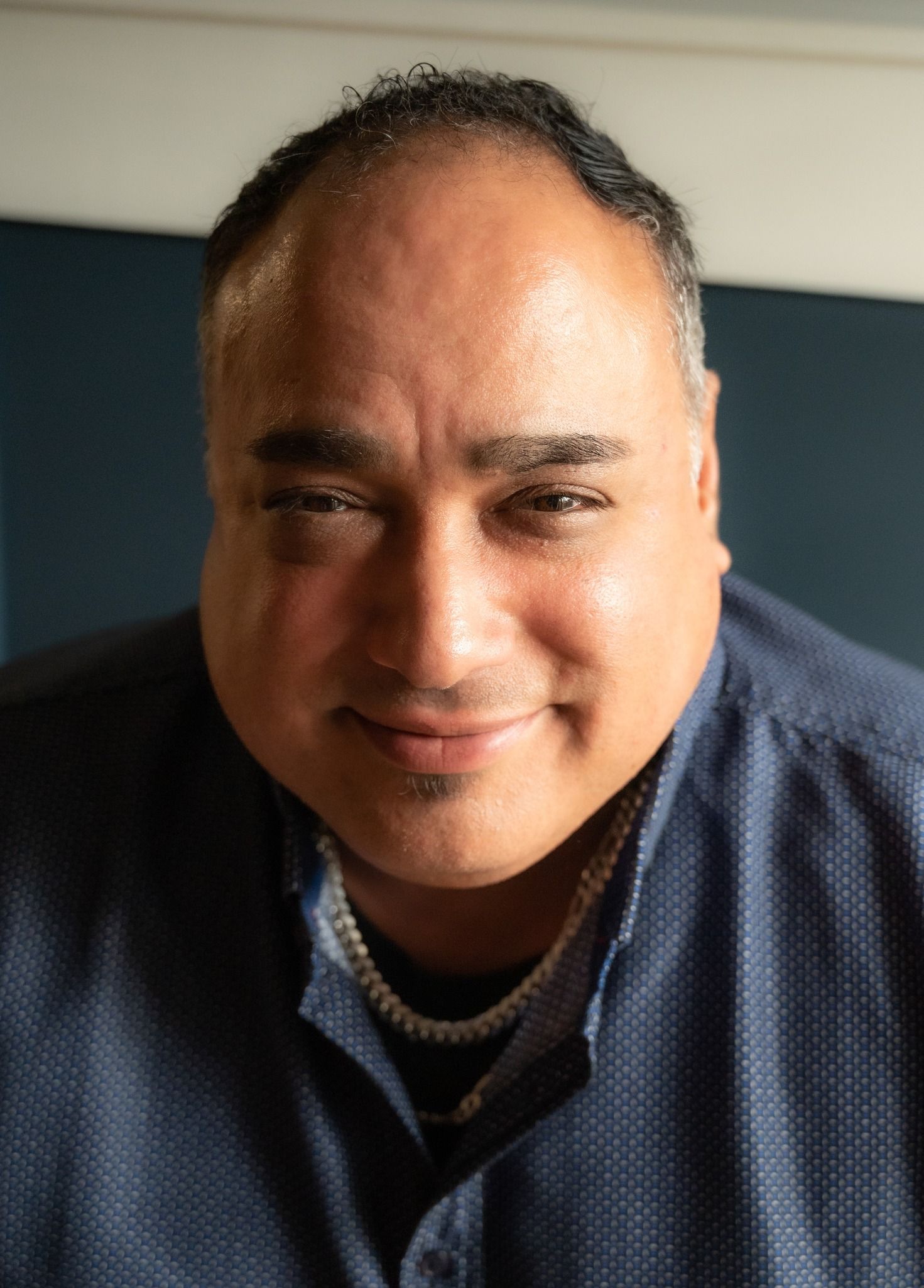 Man smiling, wearing a blue shirt, seated, looking at the camera.