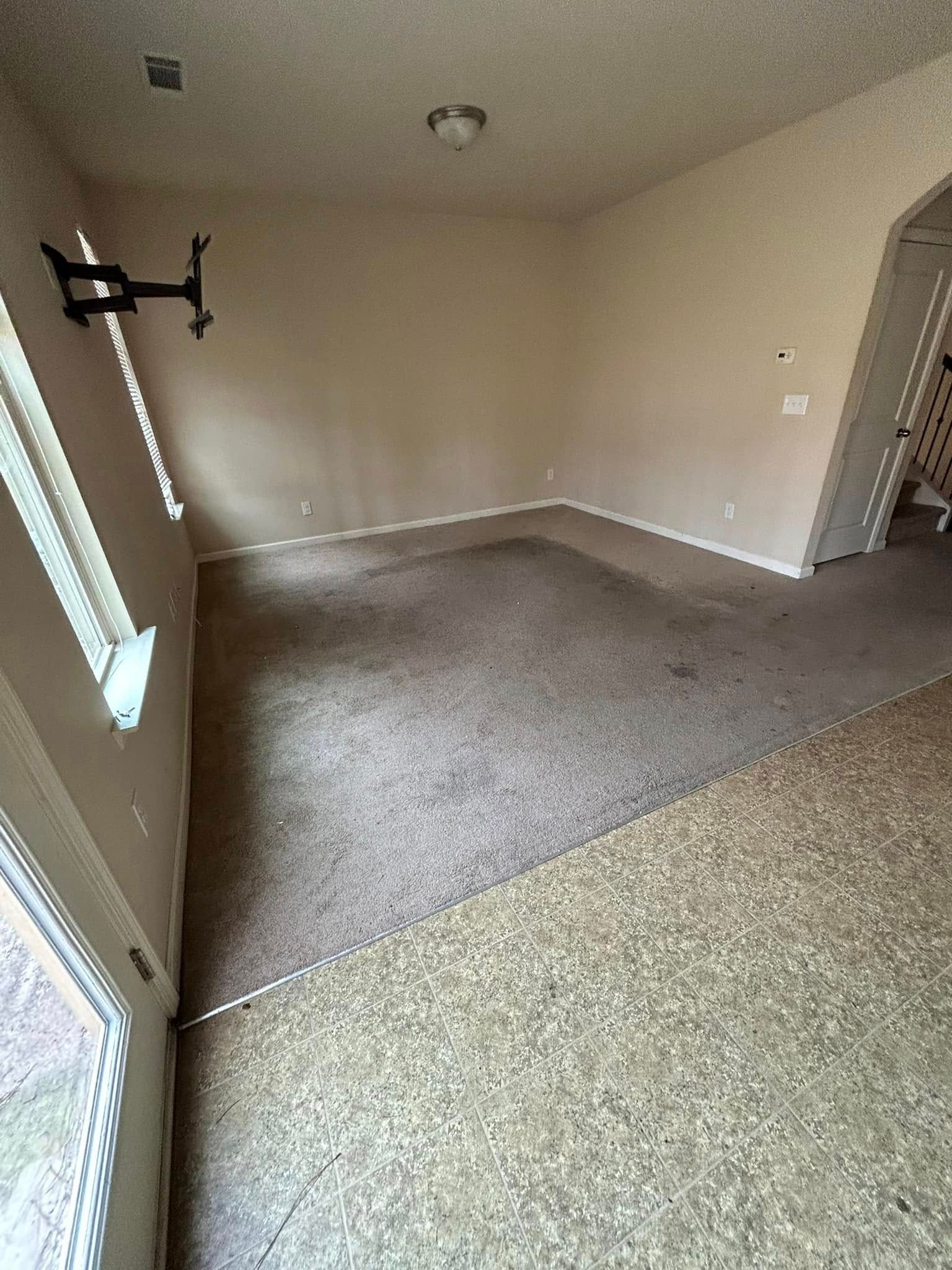 Empty room with dirty carpet, a window, TV mount on the wall, and an arched doorway.