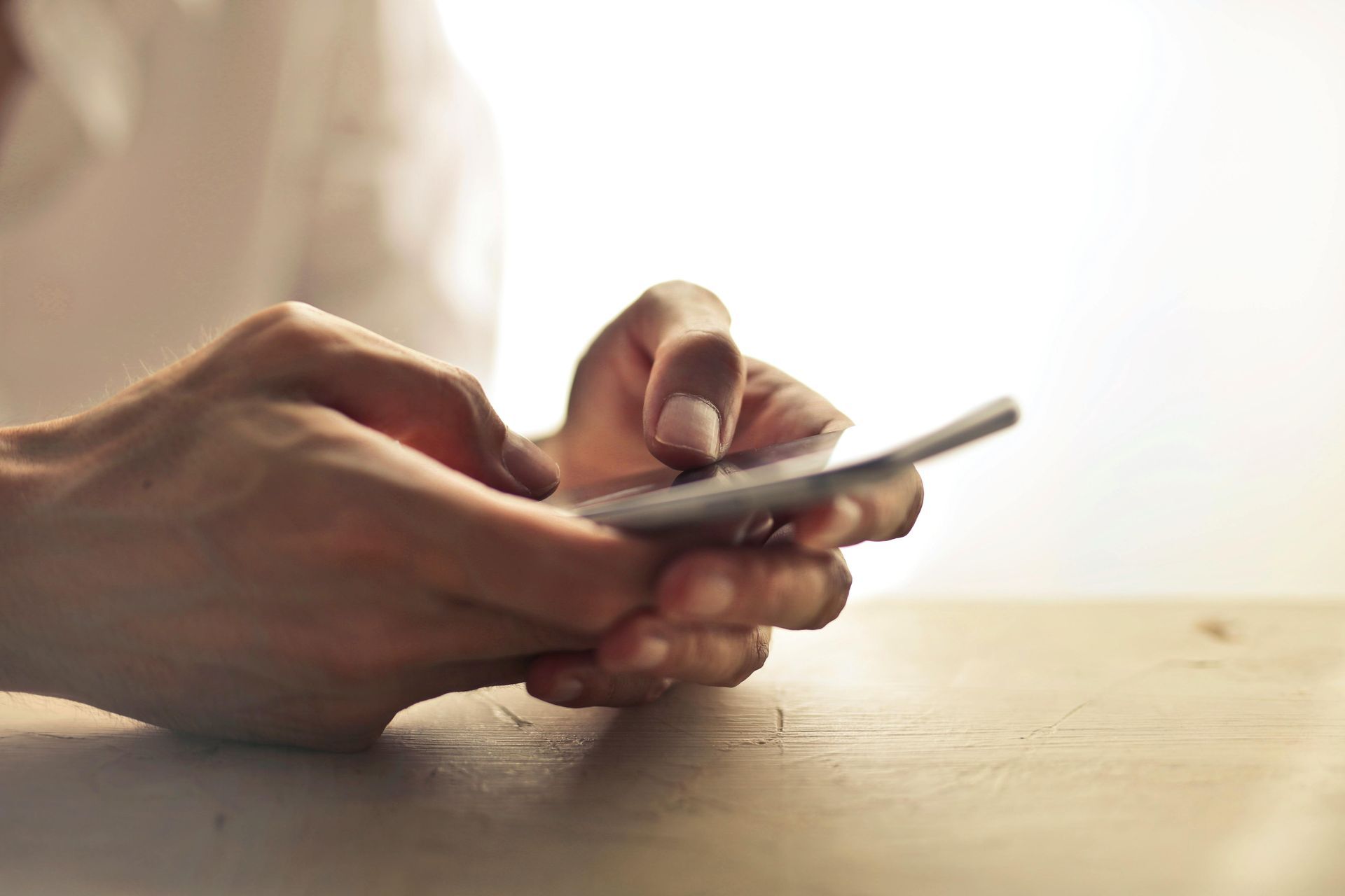 Hands holding and using a mobile phone on a wooden table.