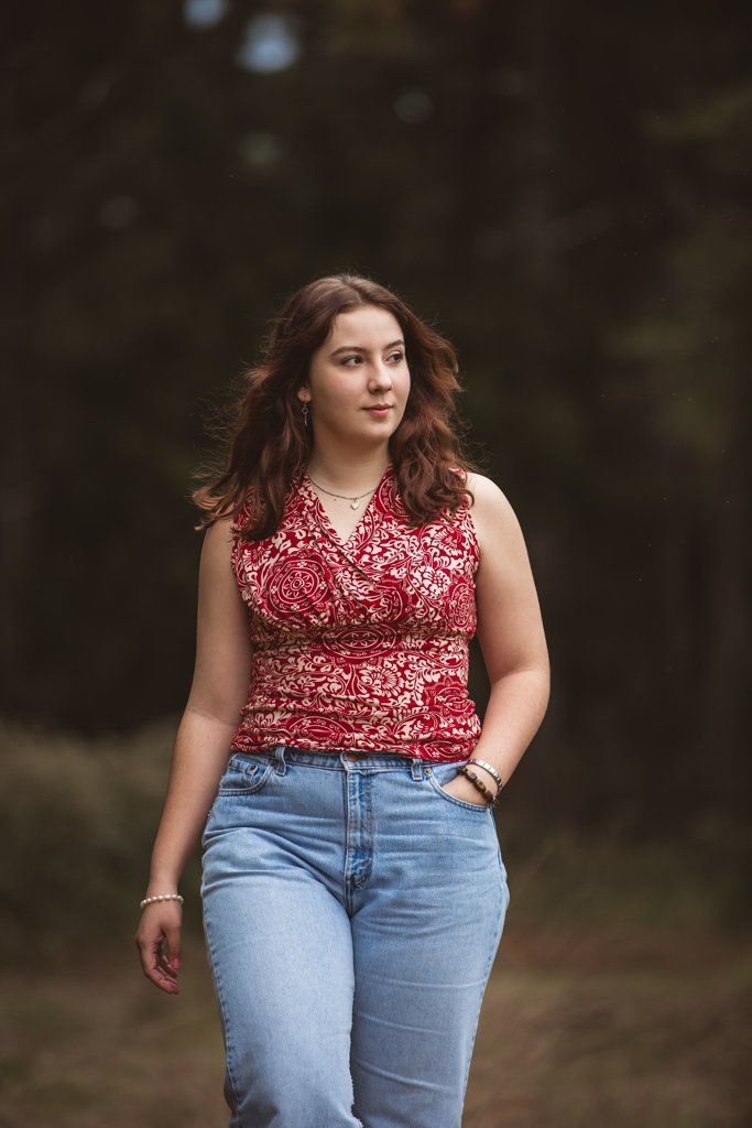 A woman in a red top and blue jeans is walking through a forest.