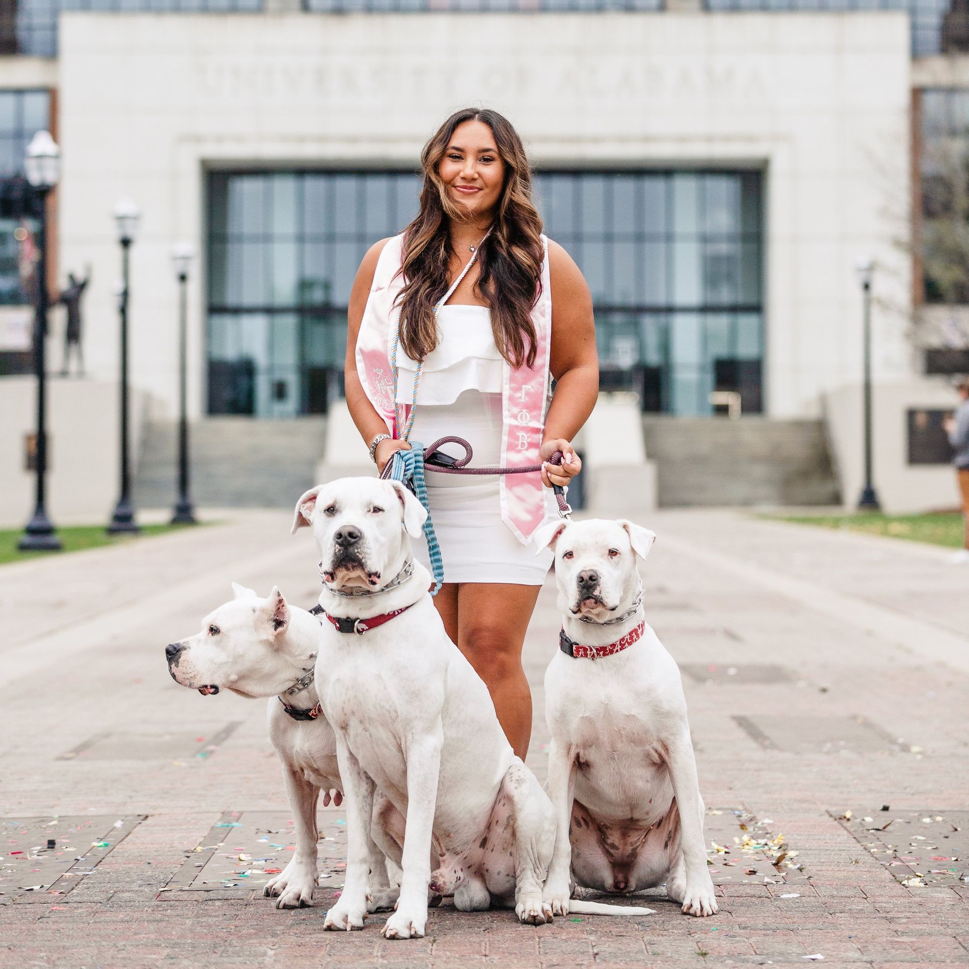 A woman is standing next to three white dogs in front of a building.