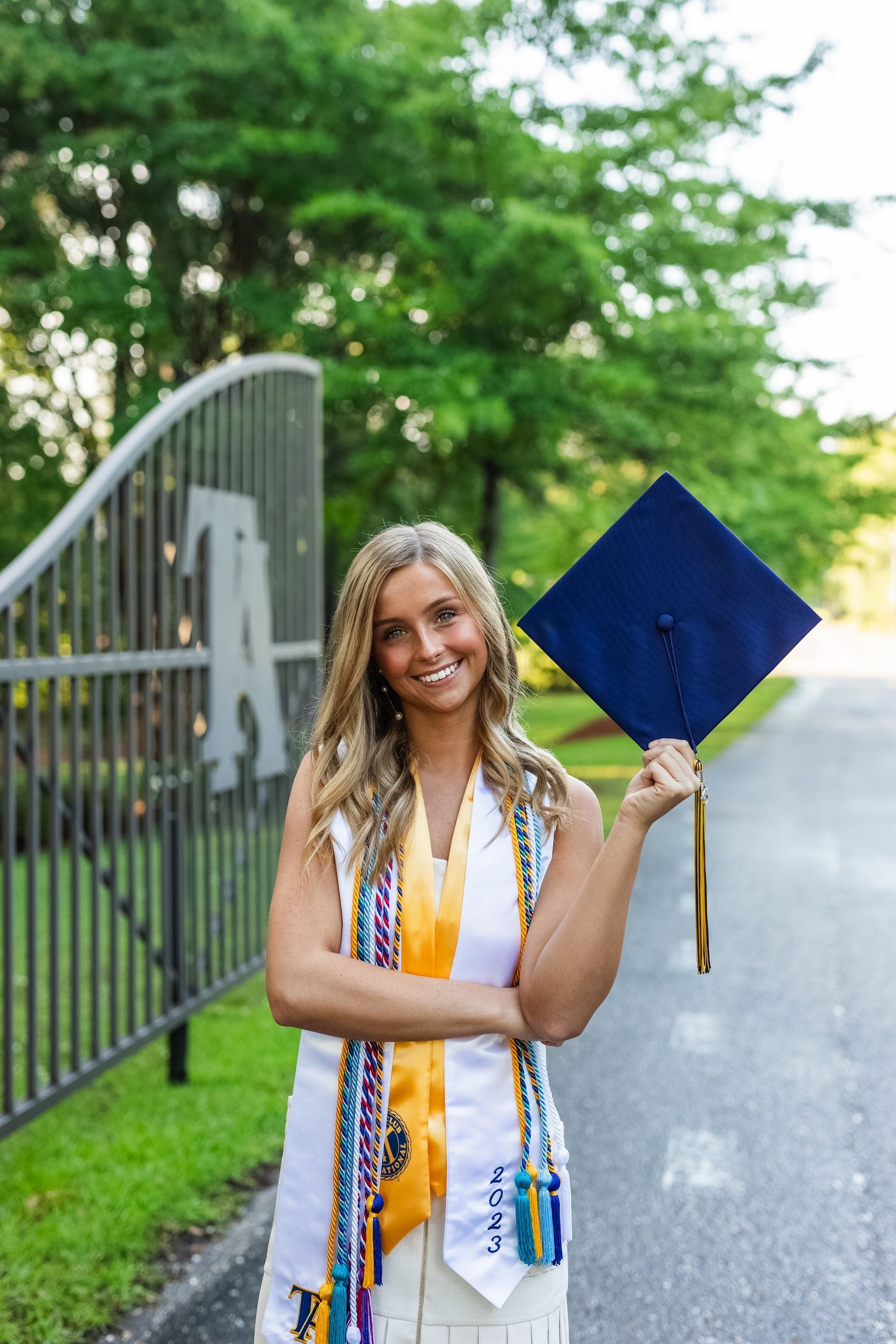 A woman in a graduation cap and gown is holding a blue graduation cap.