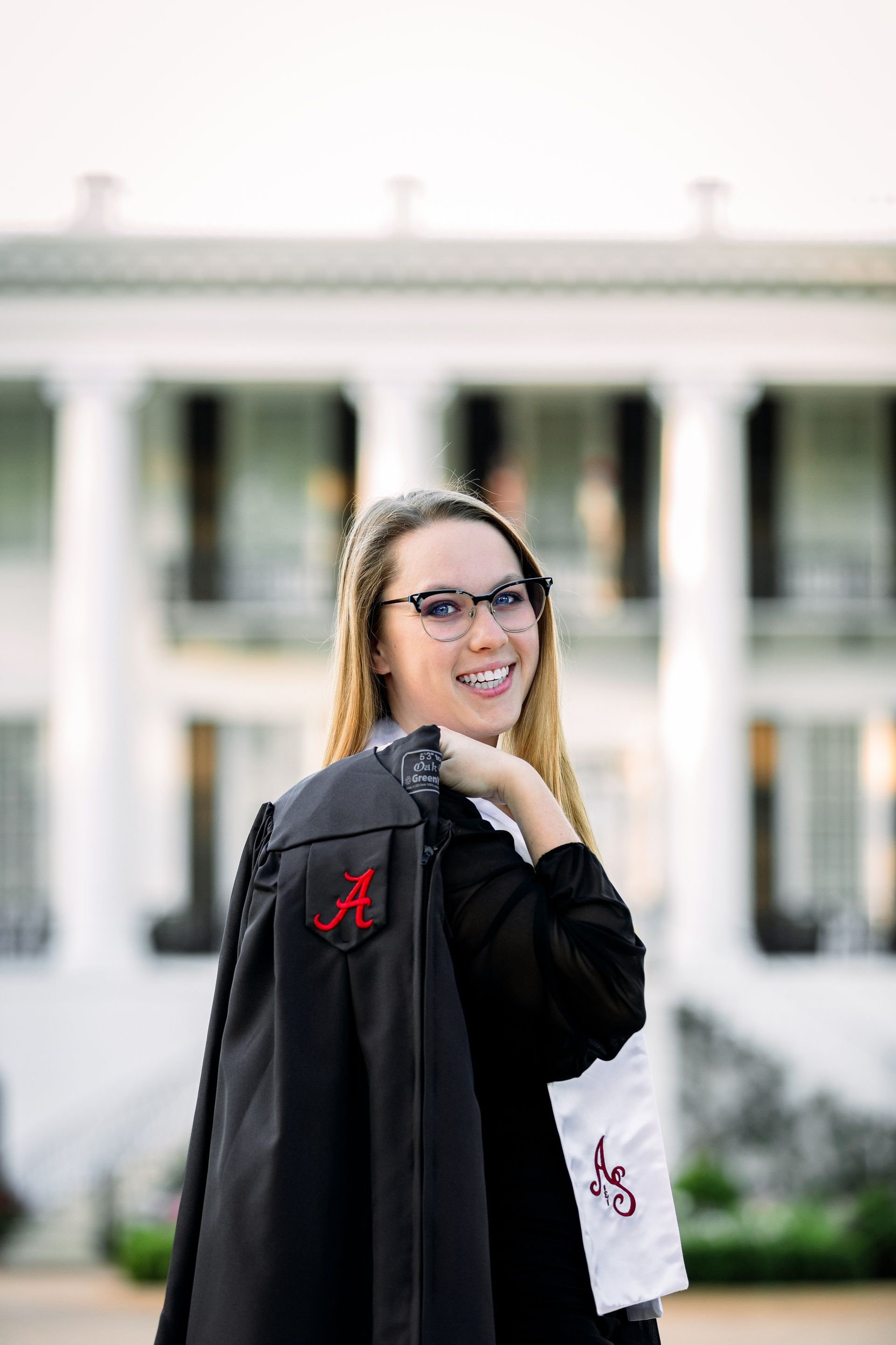 A woman in a graduation cap and gown is standing in front of a white building.
