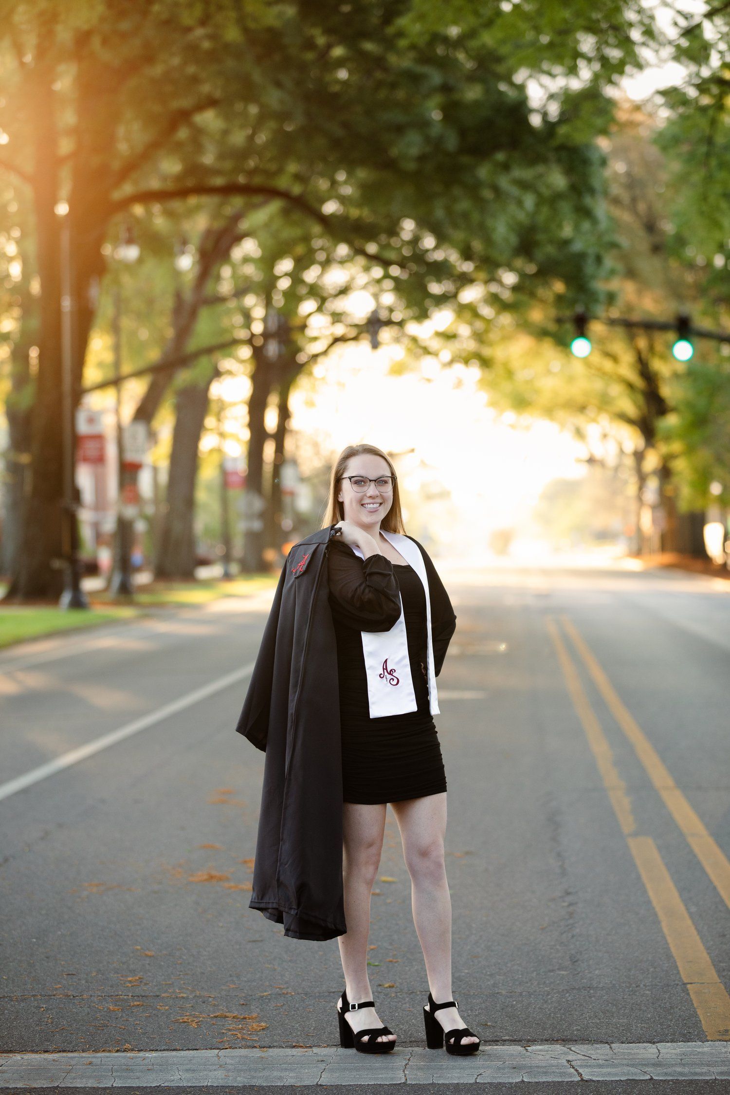 A woman in a graduation cap and gown is standing on the side of a road.
