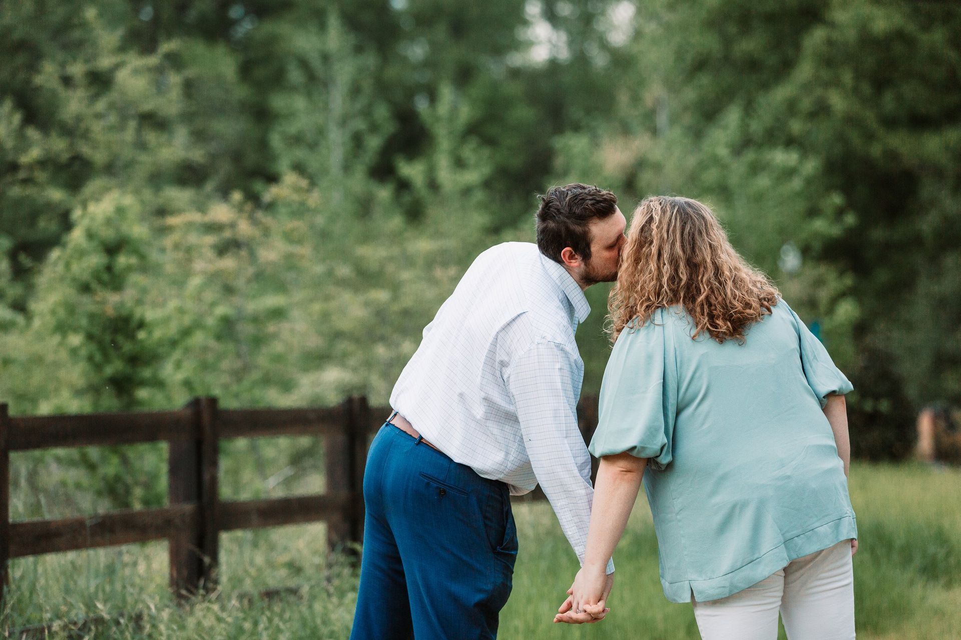 A man and woman are kissing in a field while holding hands.