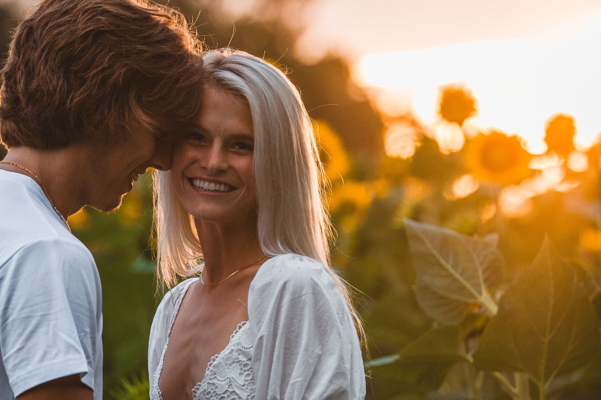 A man and a woman are looking at each other in a field of sunflowers.