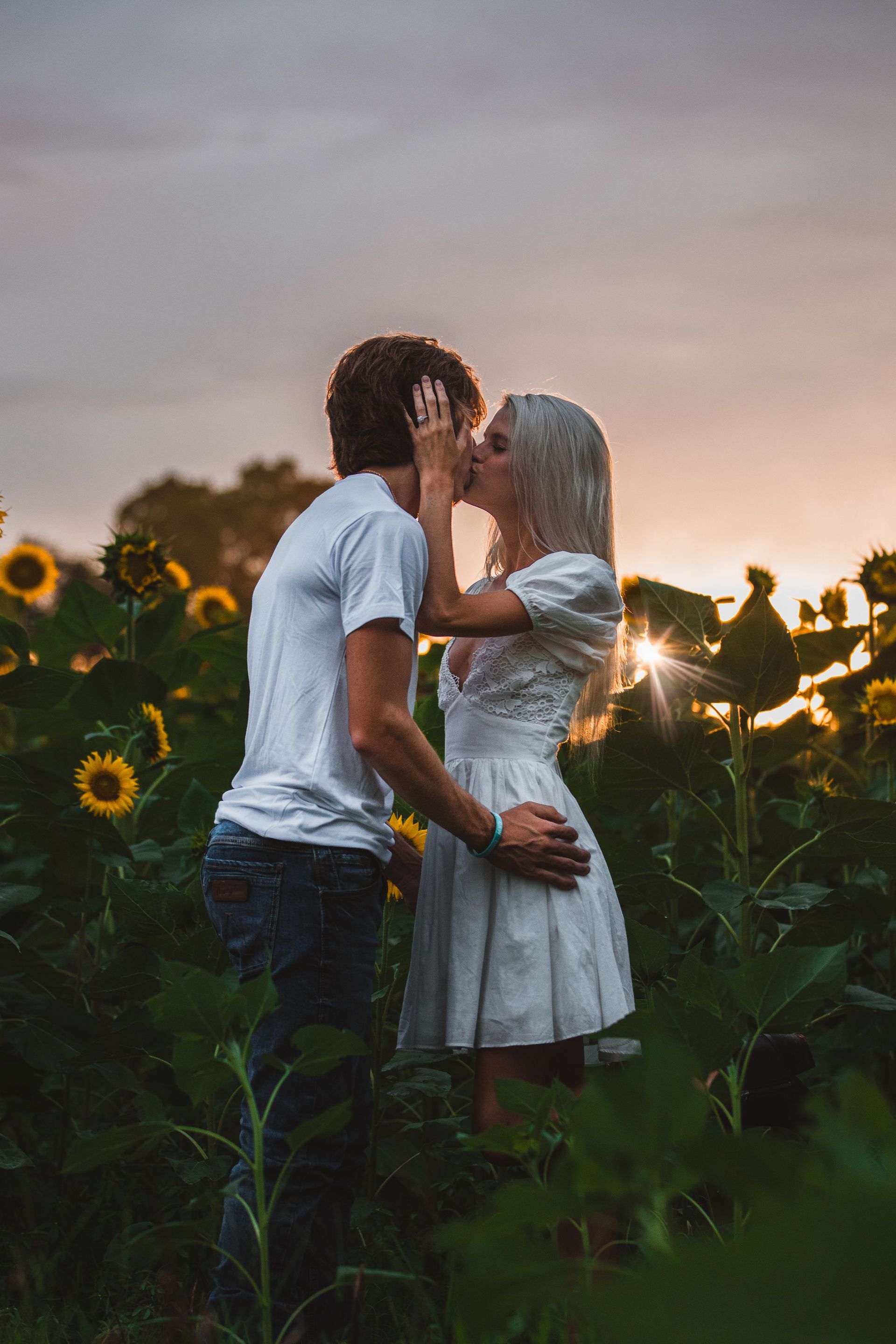 A man and a woman are kissing in a field of sunflowers.