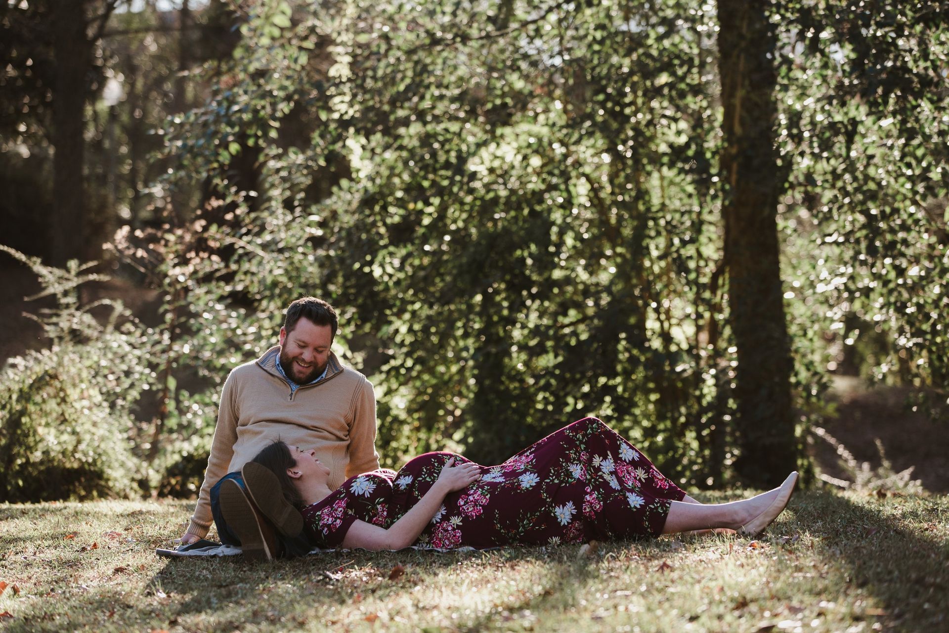 A man and a pregnant woman are laying in the grass in the woods.