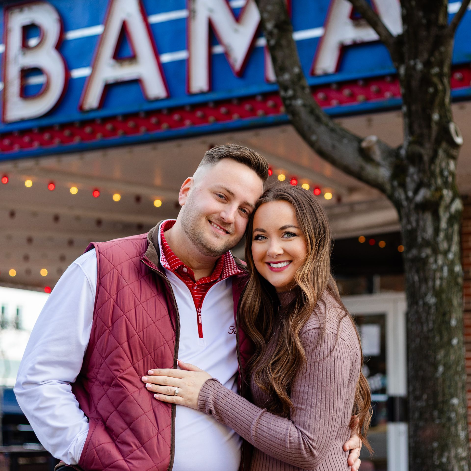 A man and woman embrace in a park under a tree in fall.