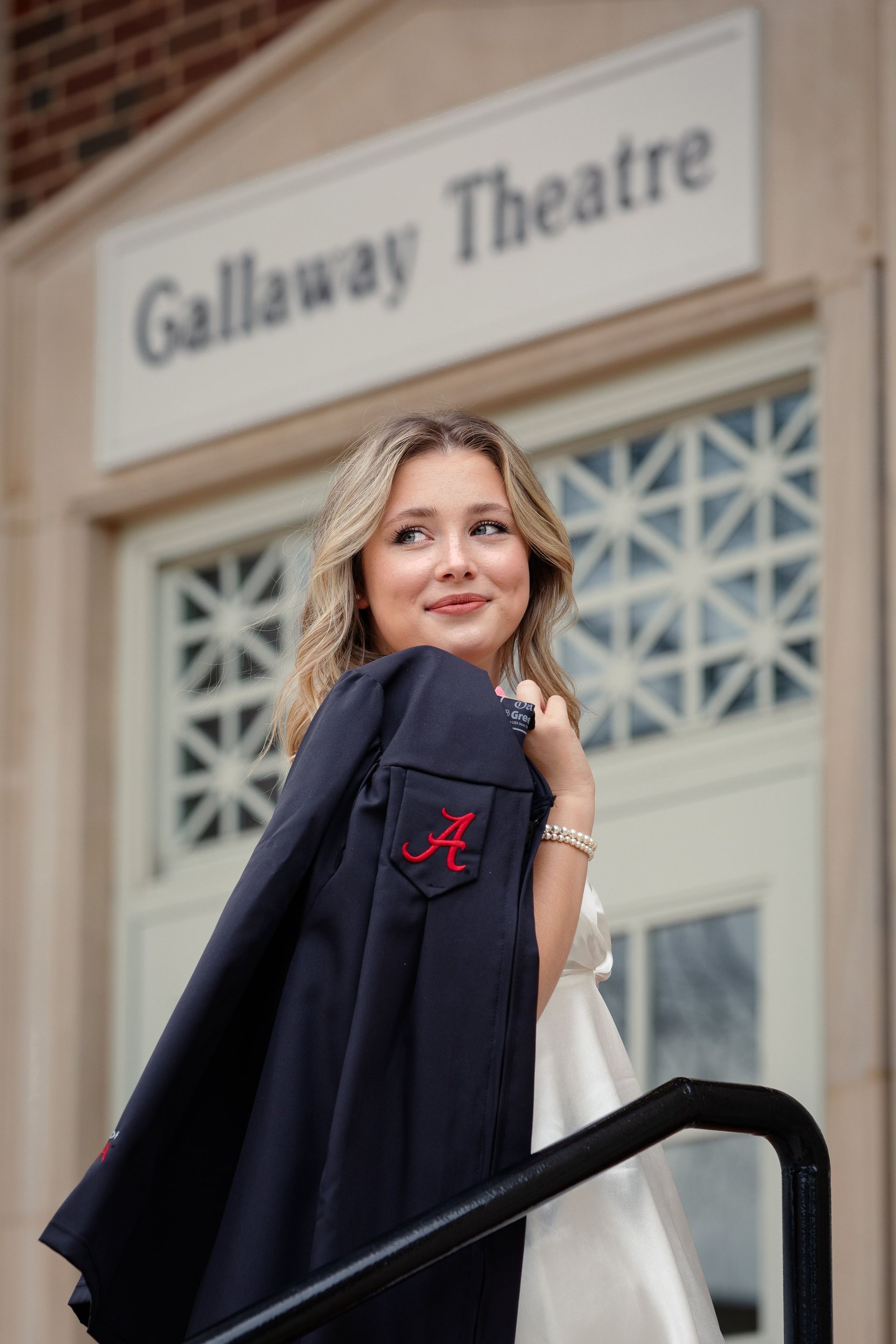 A woman in a graduation cap and gown is standing in front of a building.
