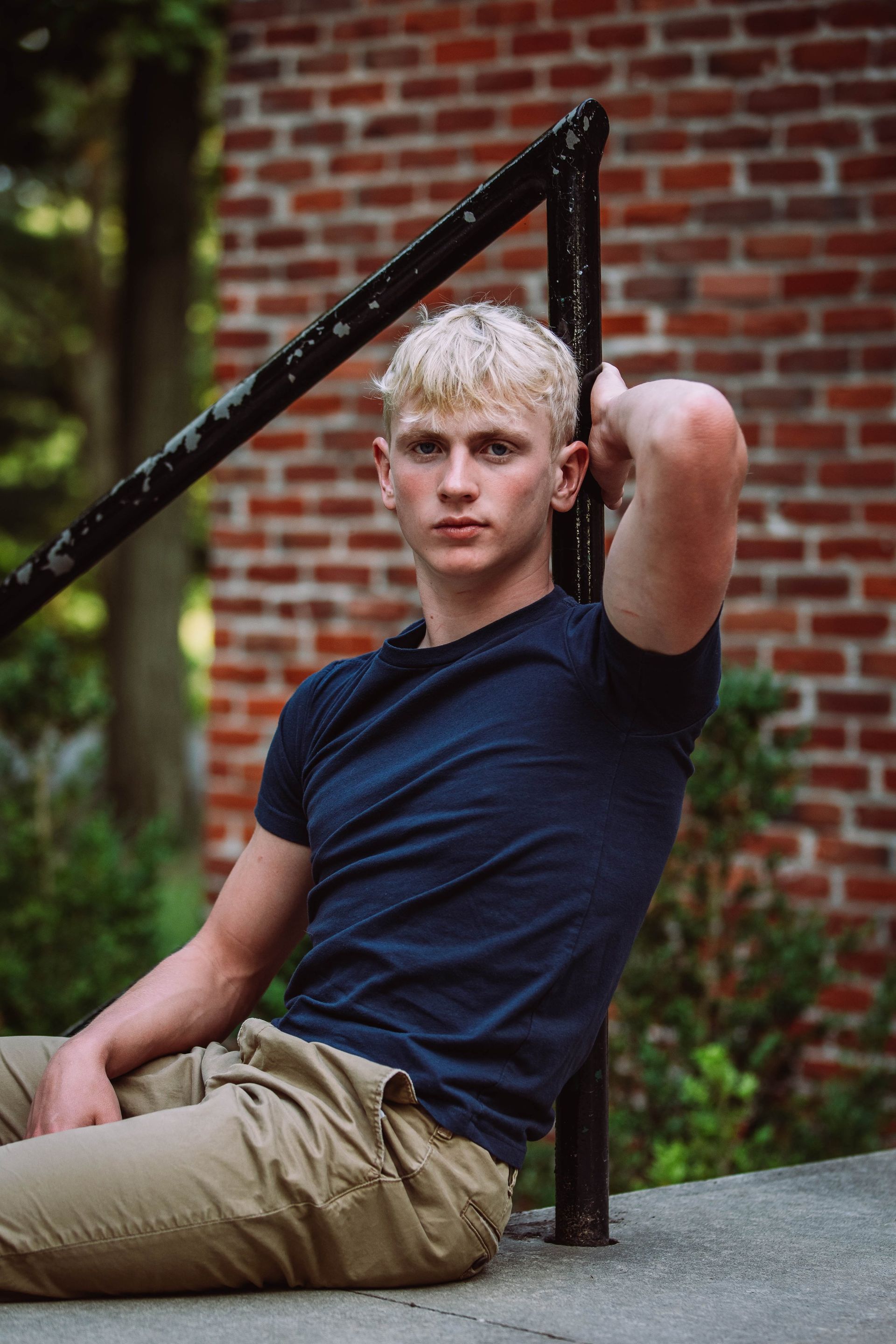 A young man is sitting on the ground leaning against a railing.