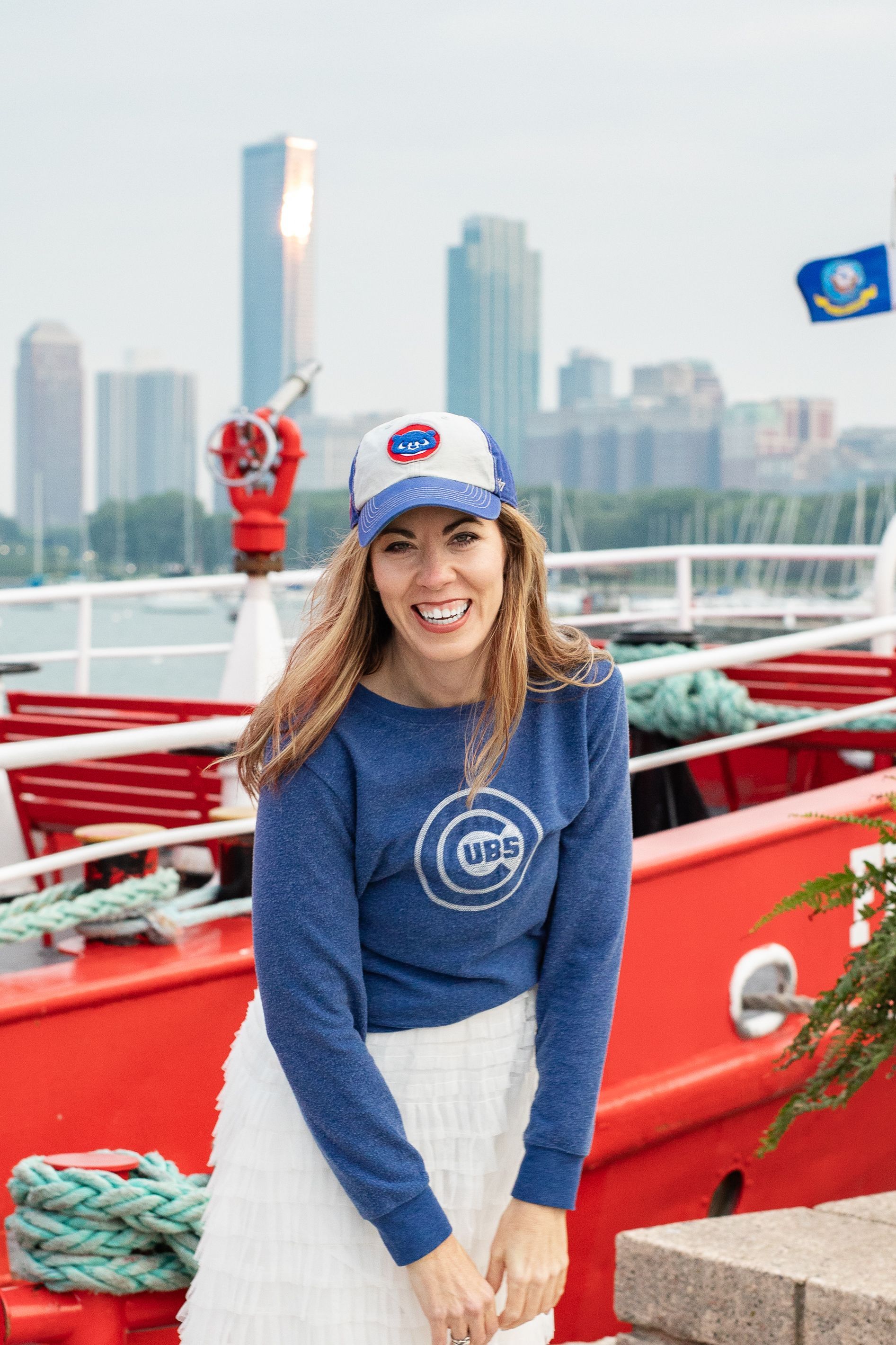 A woman wearing a blue sweatshirt and a hat is standing in front of a red boat.
