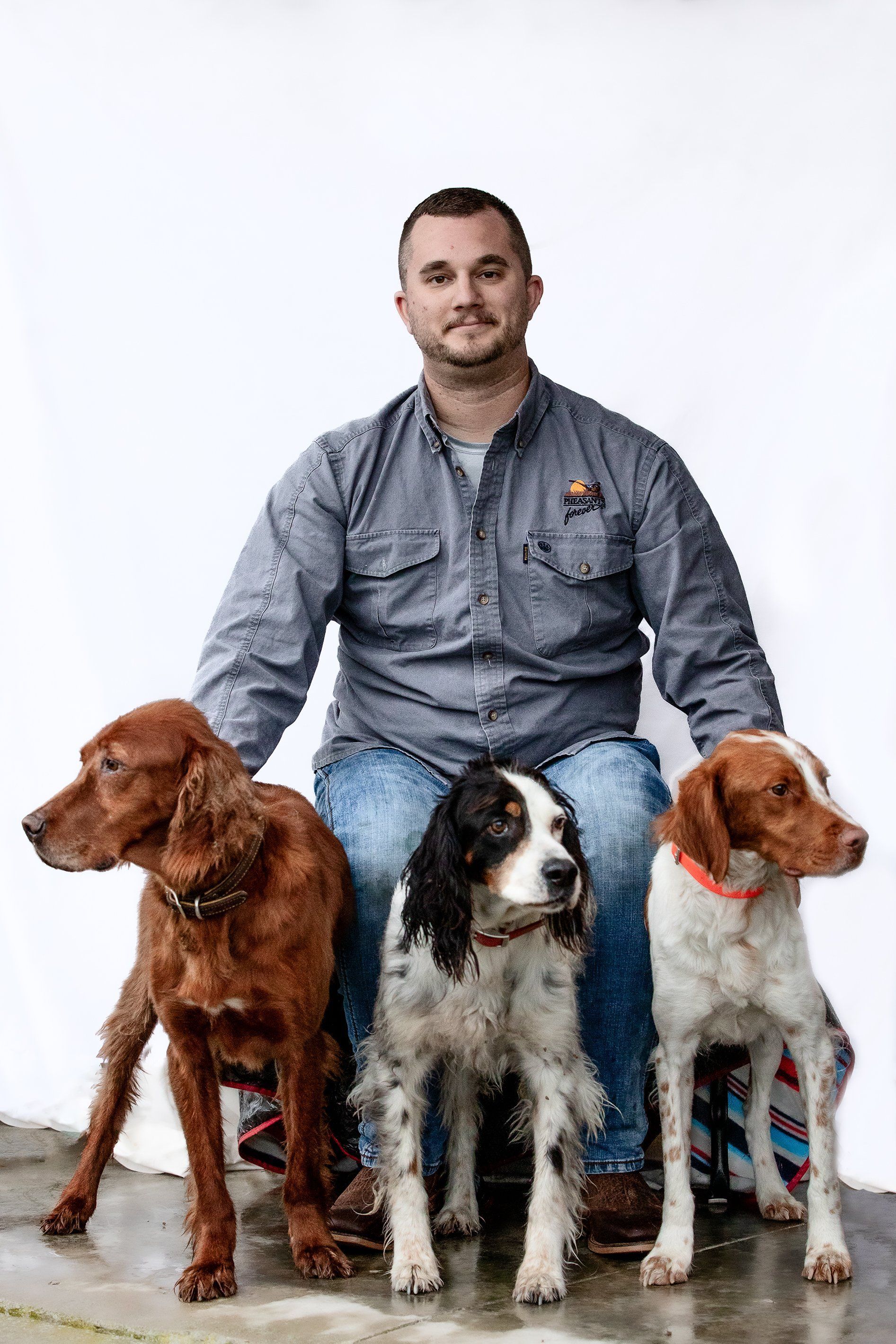 A man is sitting on the ground with three dogs.