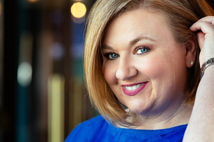 A woman in a blue shirt is smiling and holding her hair.